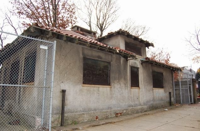 A plain stucco building with a red-tiled roof and wire gates on either side