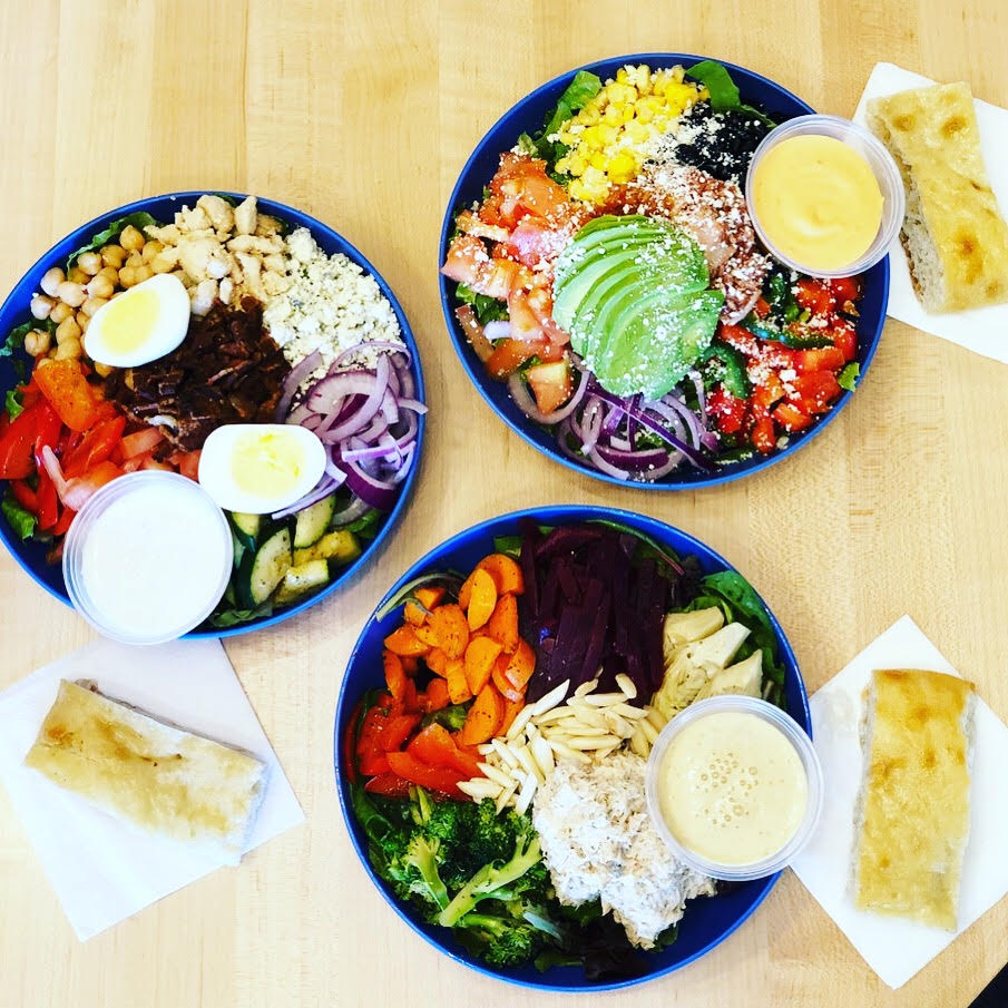 A bird’s eye view of three salads with various vegetables, such as avocado, corn, broccoli, and red peppers.
