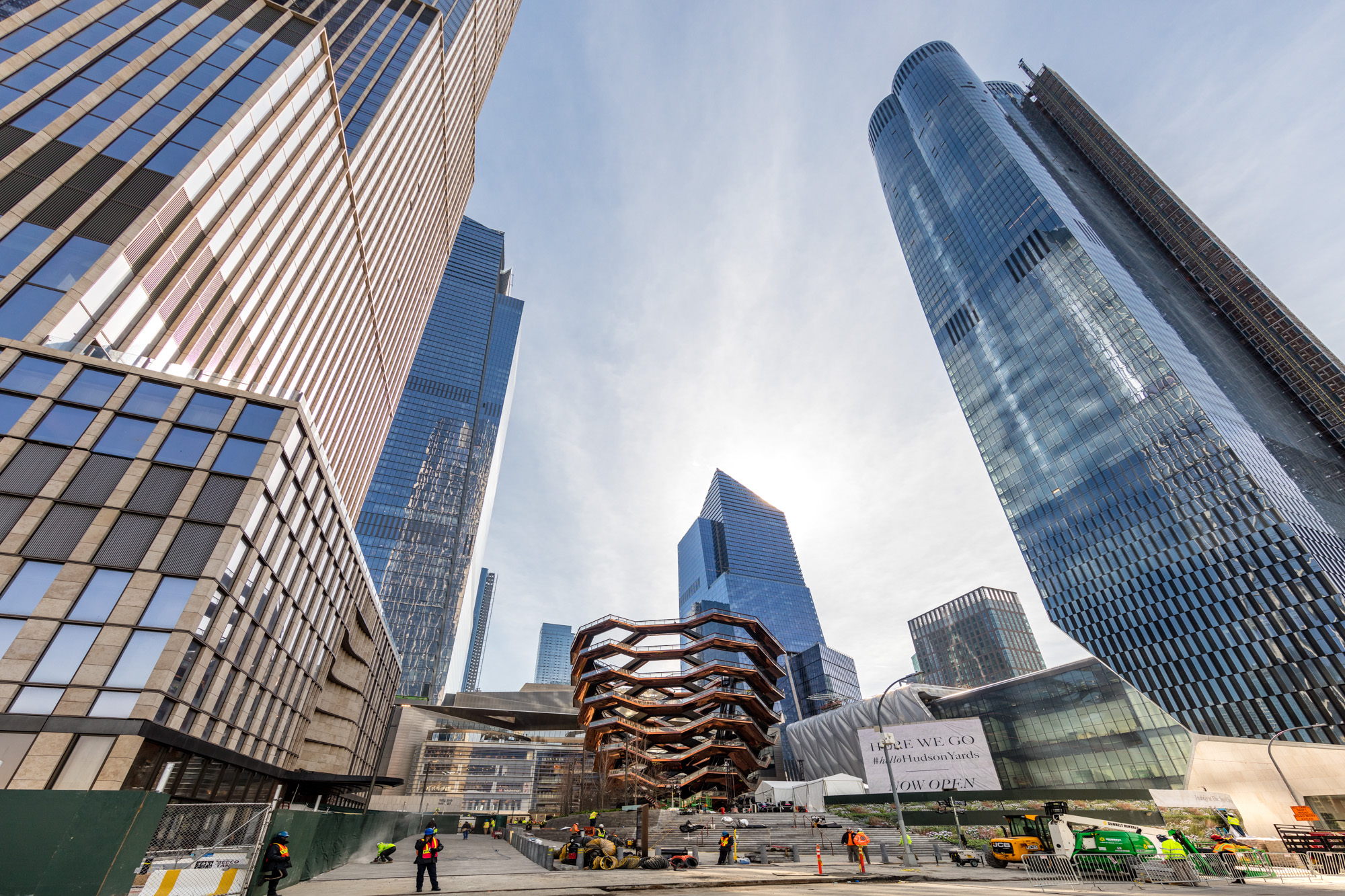 Several tall buildings with glass facades surround a landmark that is shaped like a beehive and made from steel. 