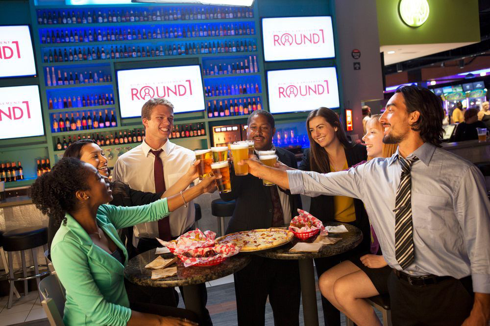 A group of friends raise their beer glasses for a toast at the all-ages arcade and games center.