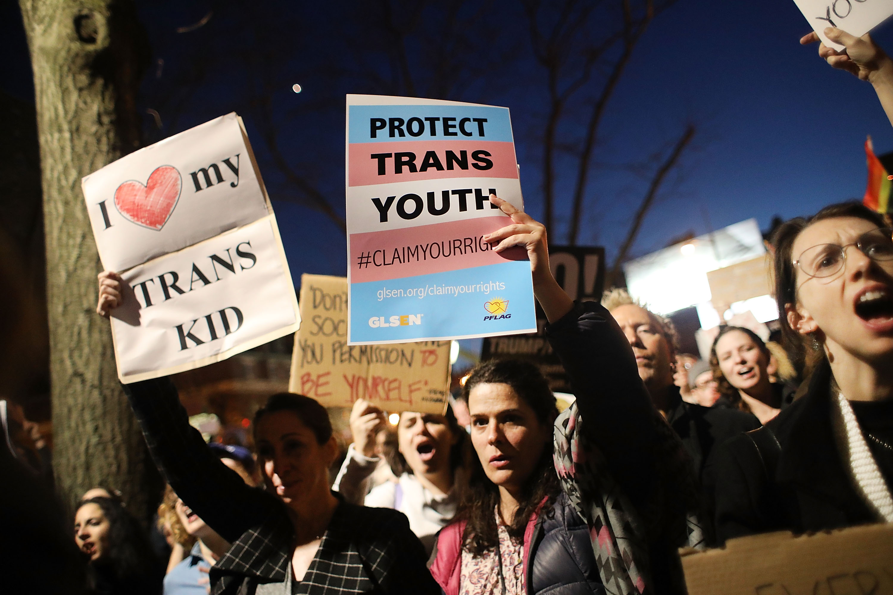 Protesters hold signs that read “I heart my trans kid” and “Protect trans youth.”