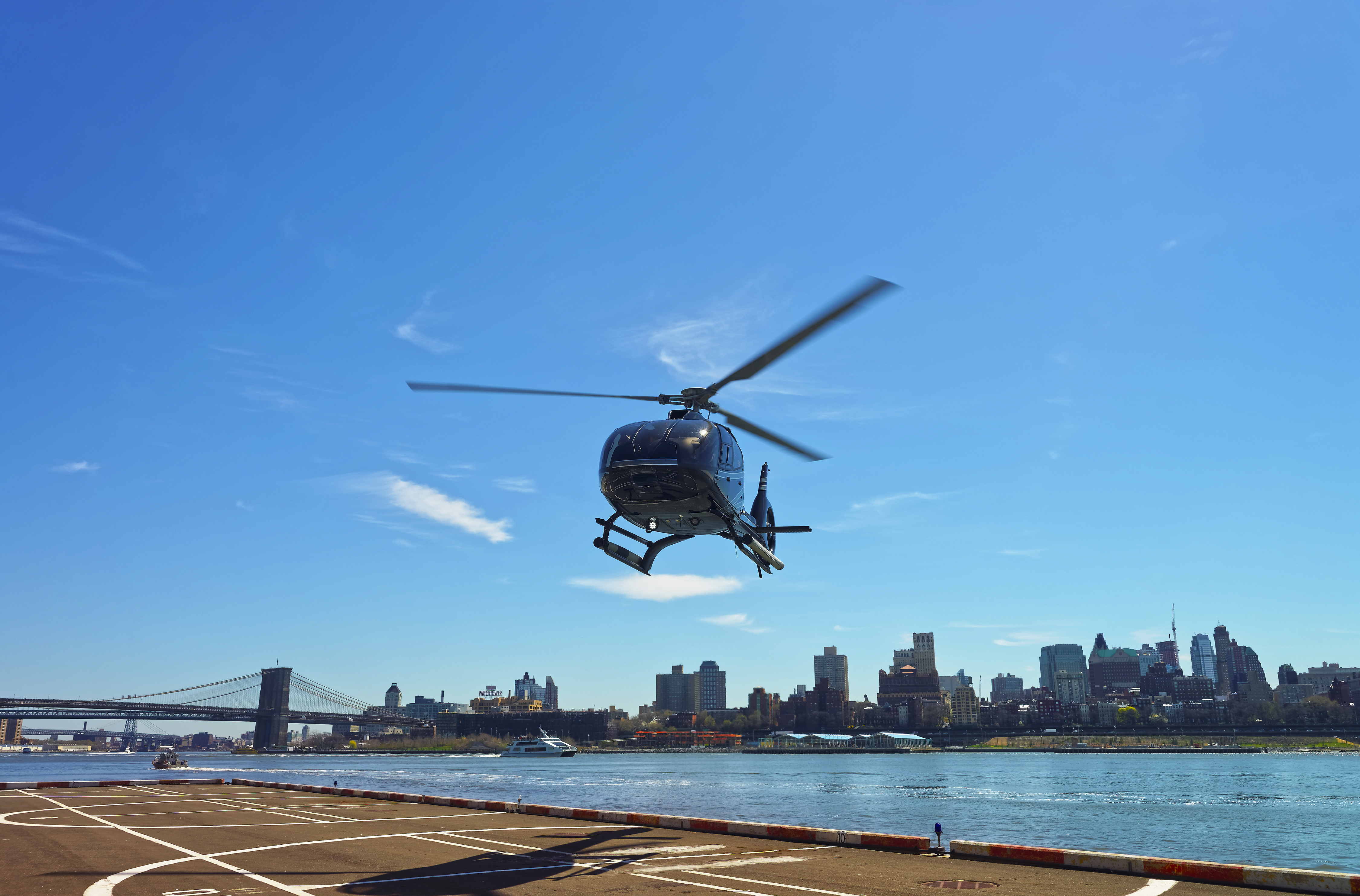 A helicopter landing in a heliport, the Manhattan and Brooklyn skylines behind it.