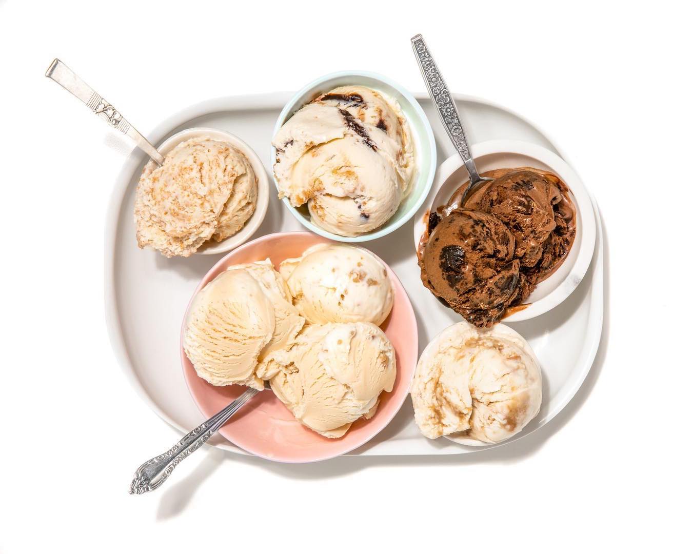 Scoops of various ice creams in various bowls and plates with spoons