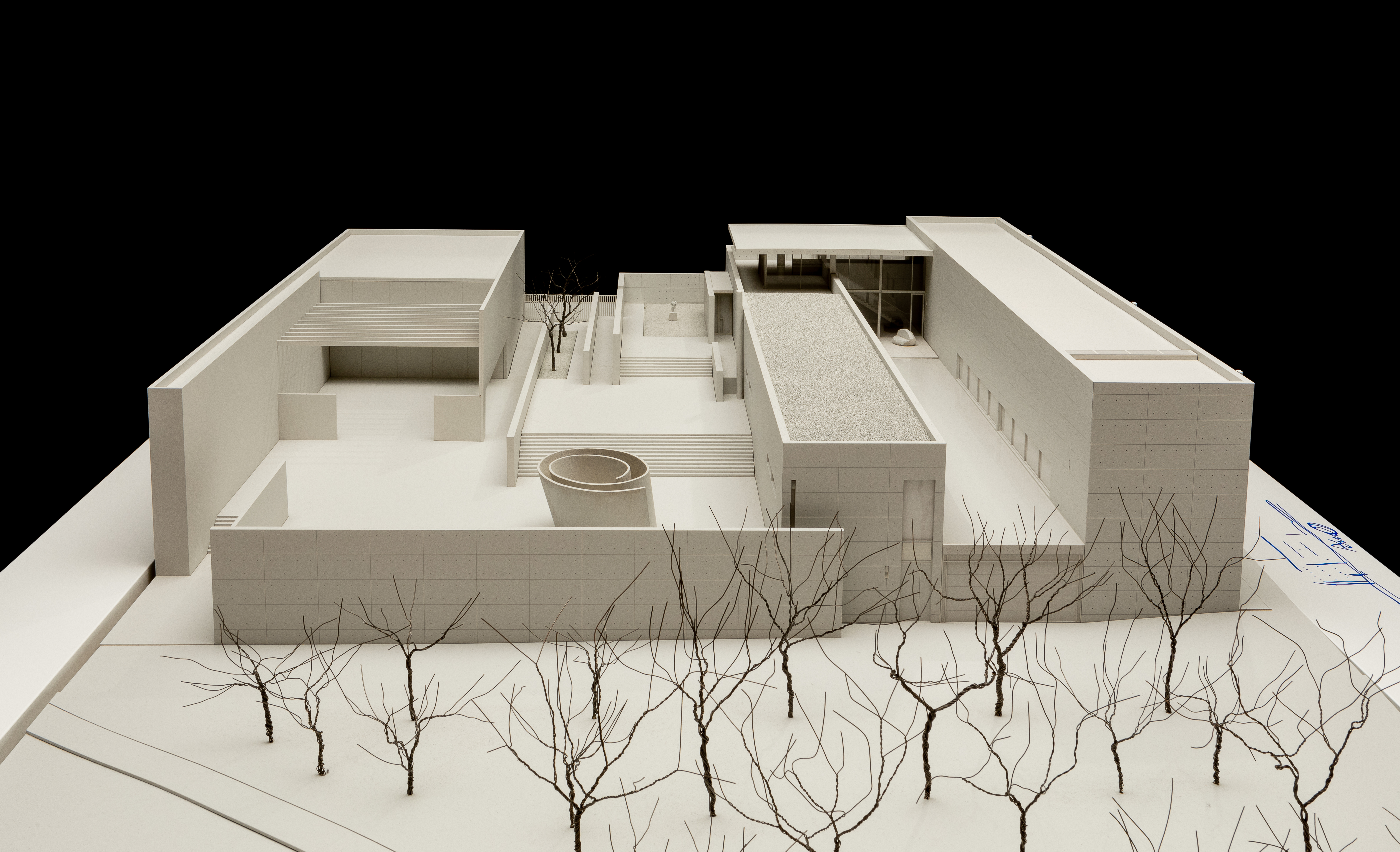 A structural, geometric white one-story model with long rectangular structures and leafless trees in the front courtyard.