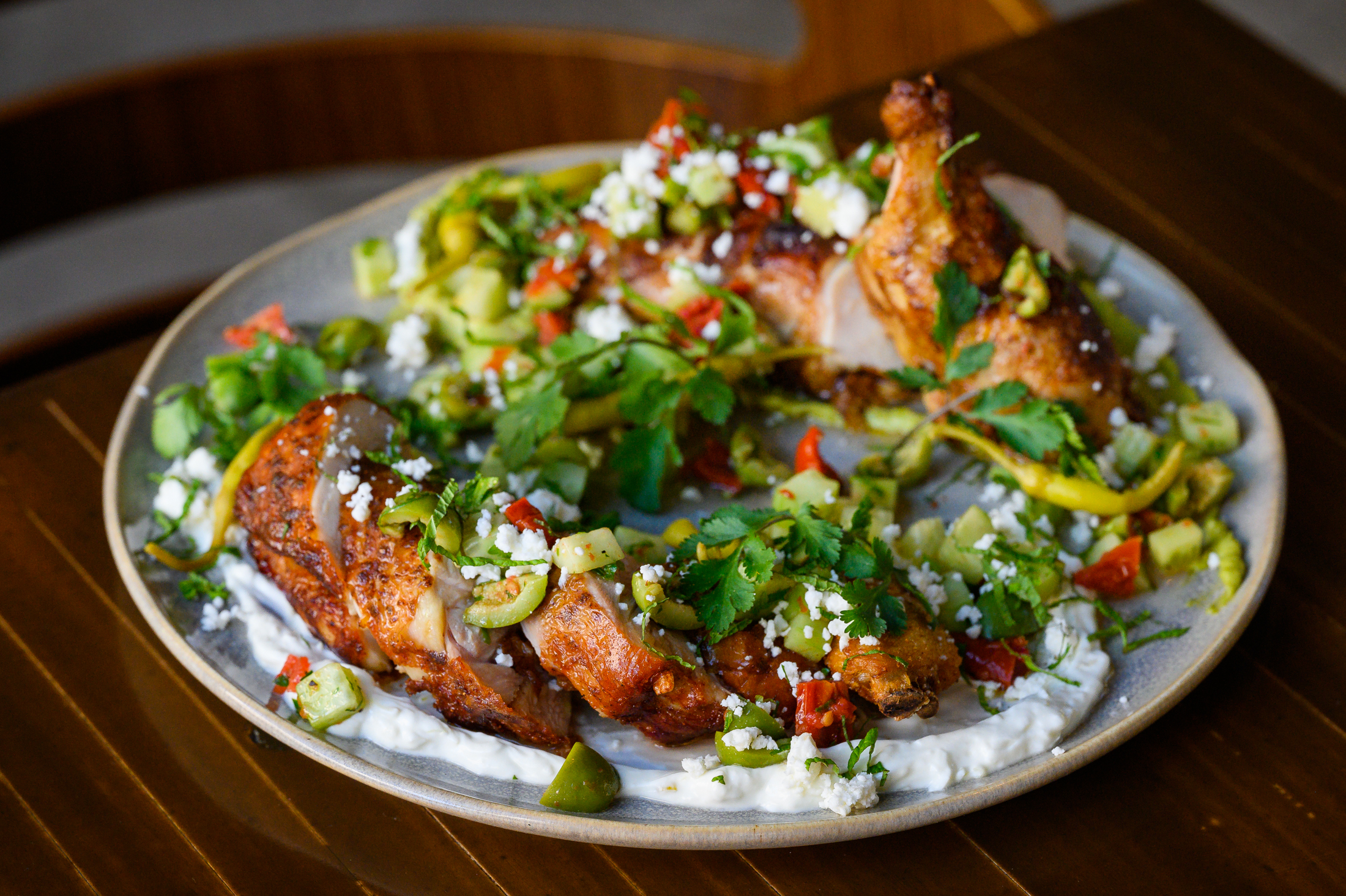 A broken-down whole roasted chicken sits on a swab of green garlic labneh with a sprinkle of spring vegetables at Arden.