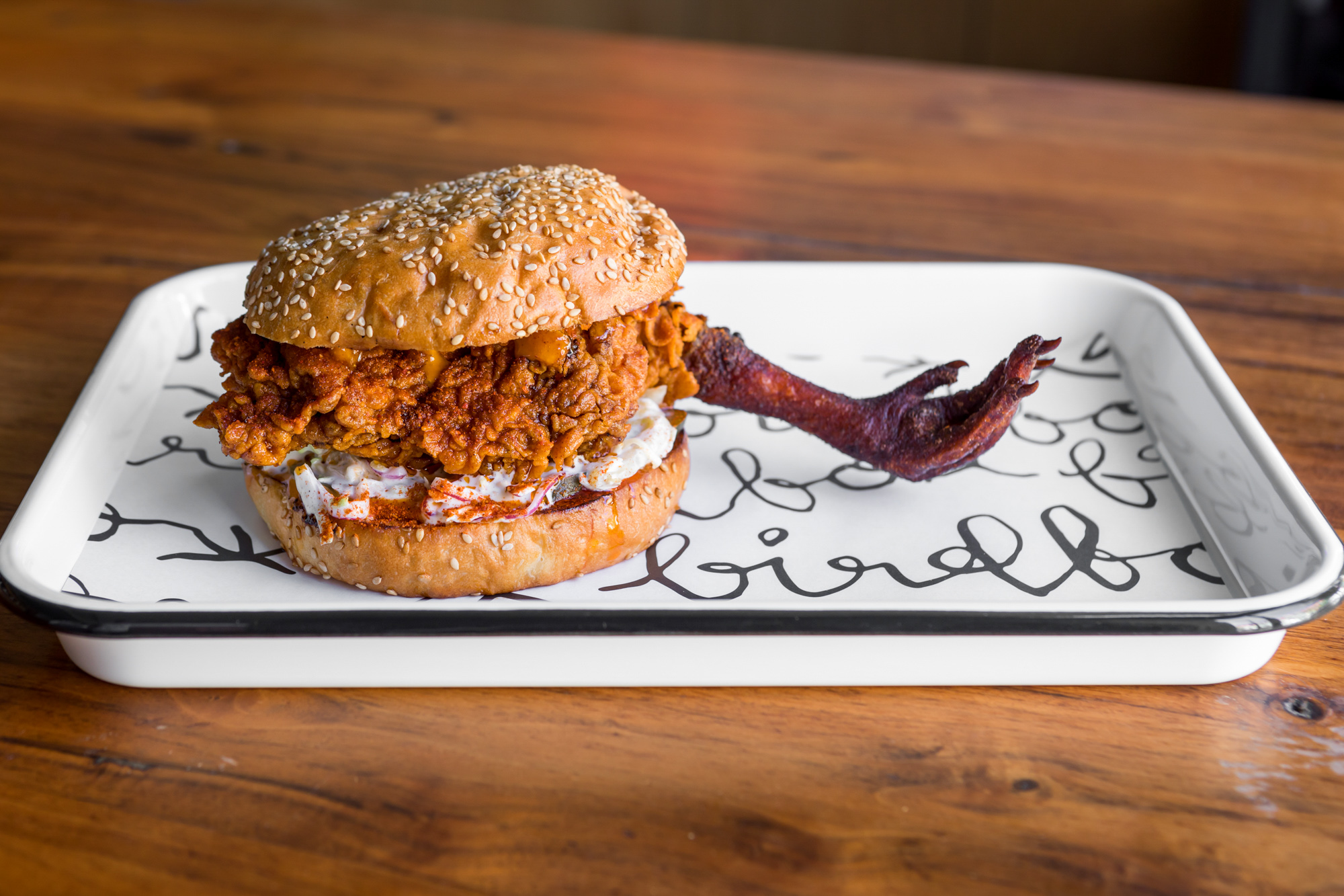 A fried chicken sandwich with a claw attached on a white tray.