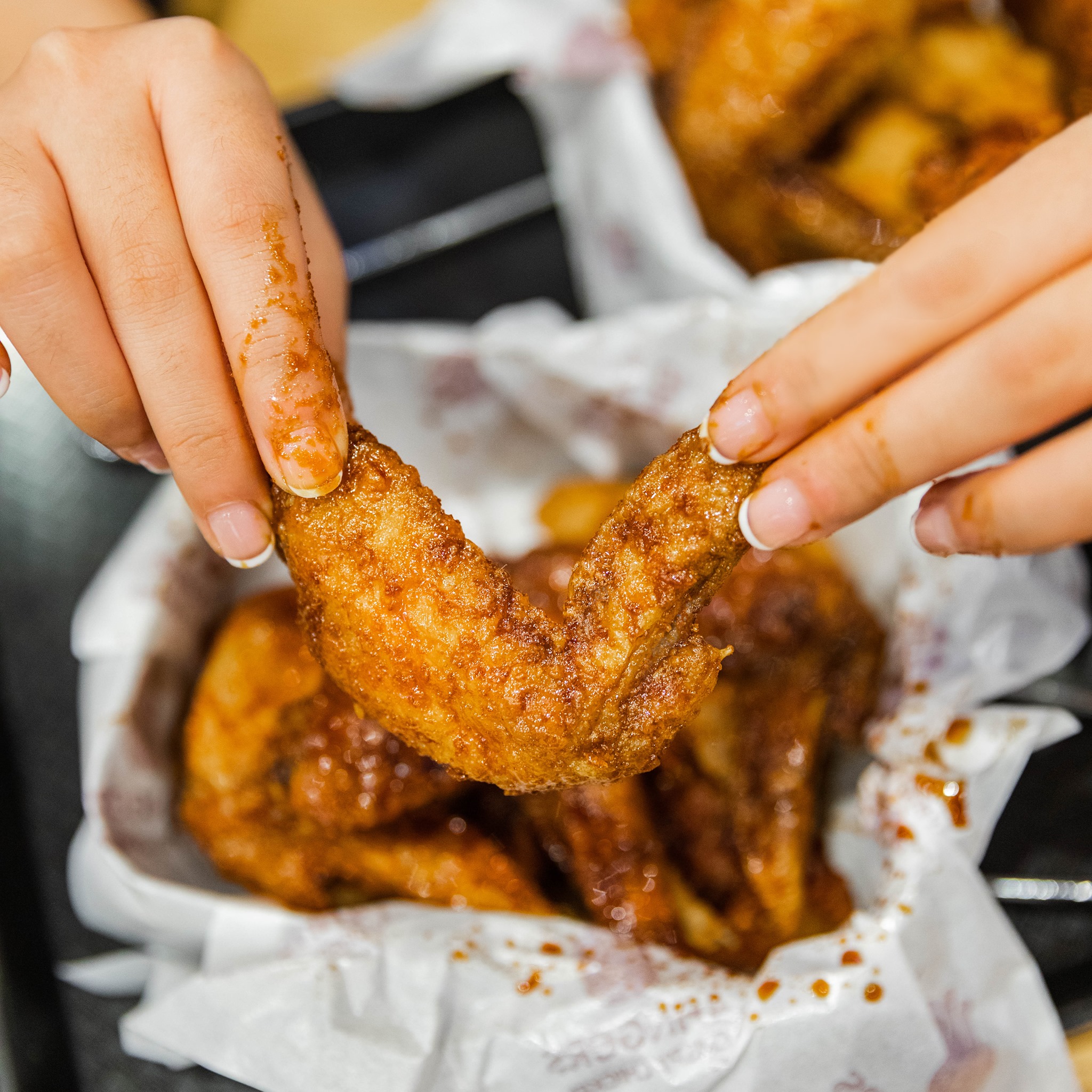 Manicured hands getting saucy while eating wings.