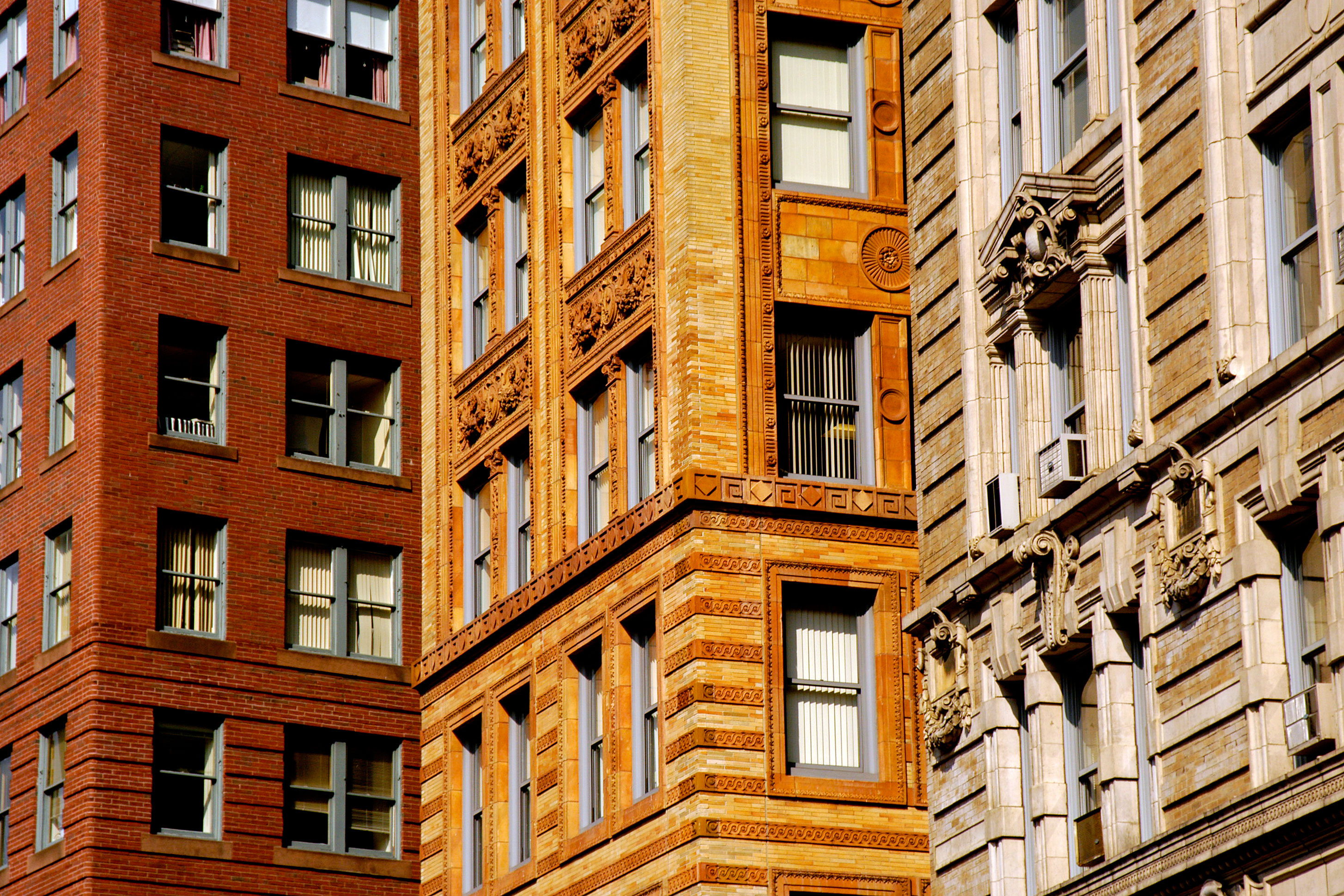 The exteriors of three apartment buildings in Boston. The center facade has orange brick. The facade on the left is red brick. The facade on the right is tan and white.