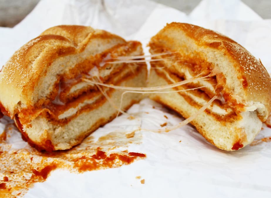 A chicken parm sandwich cut in half with stringy cheese stretched between the two halves. 