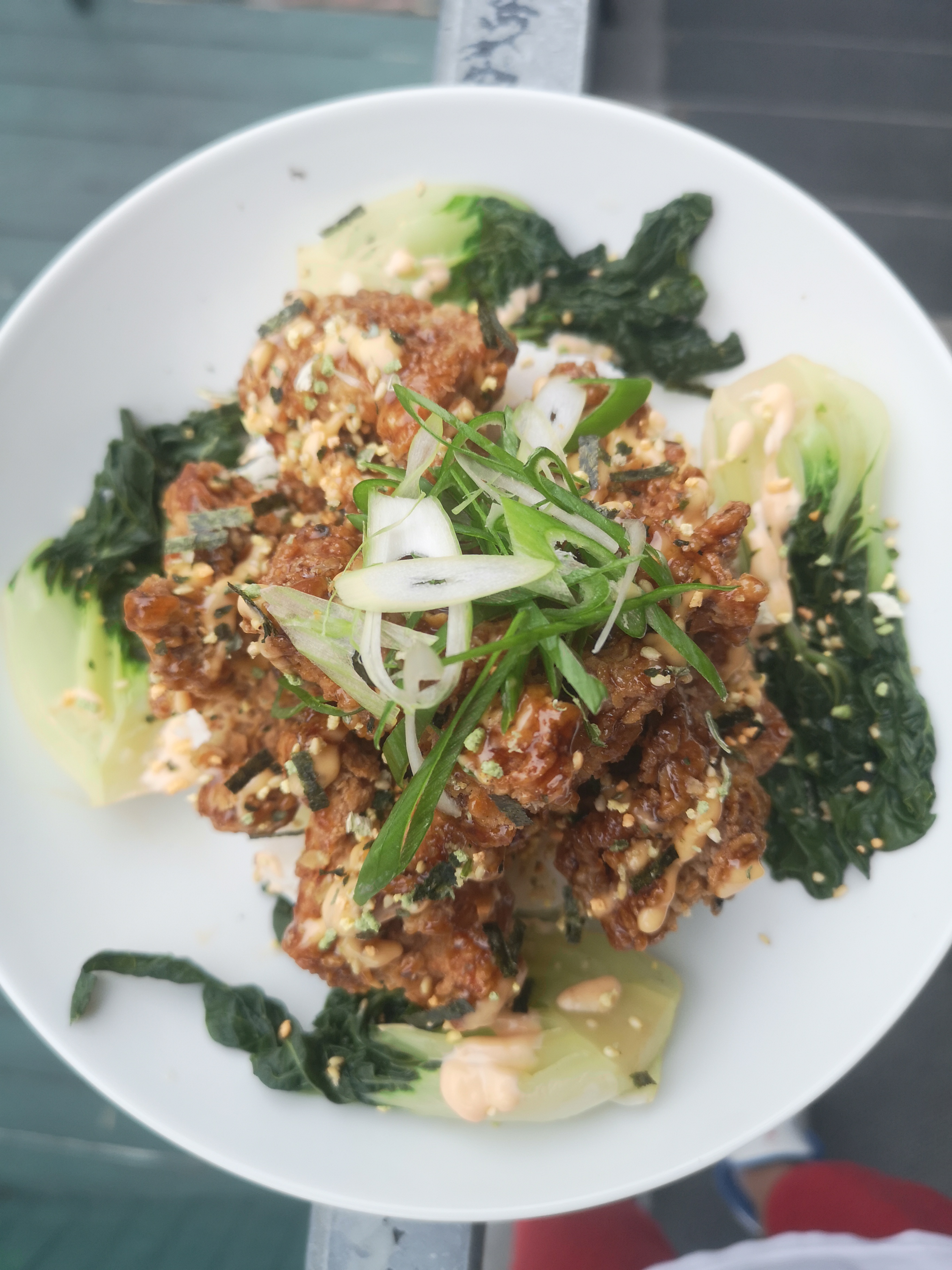 A white bowl of fried furikake chicken with bok choy beneath and green onions on top.