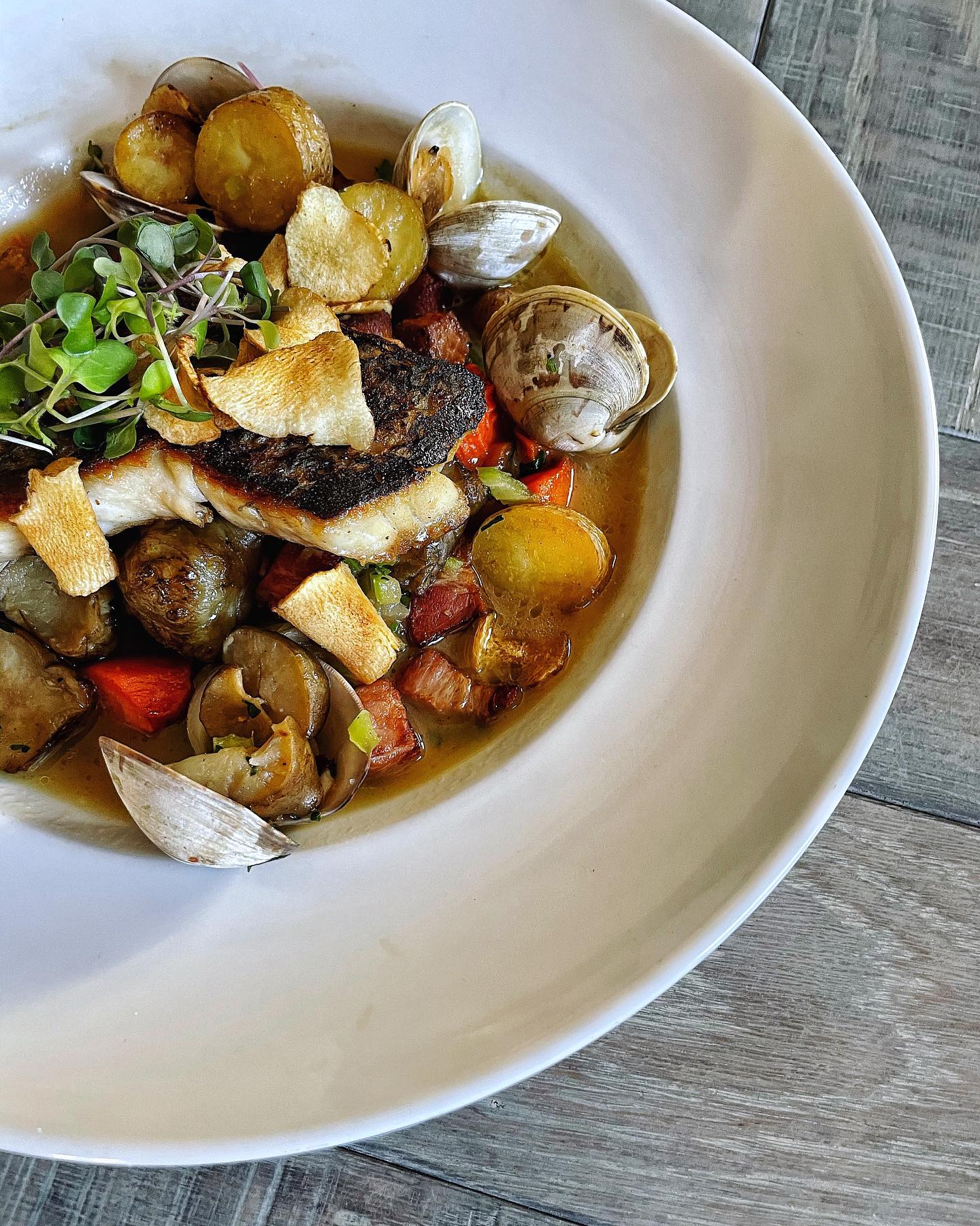 A bowl of chowder with clams, sunchokes, and potatoes garnished with herbs and sun-dried tomatoes from Table and Main in Roswell, GA