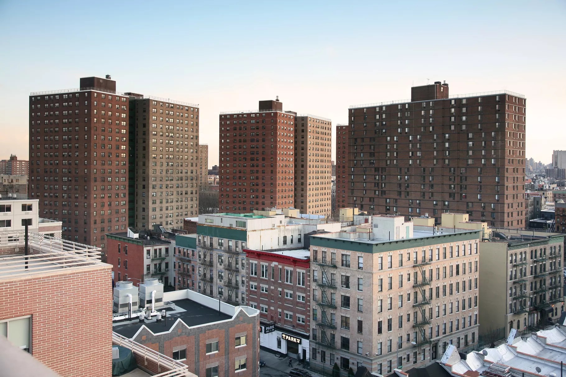 Three brown, high-rise public housing buildings loom over a handful of white low-rise apartment buildings in Manhattan.