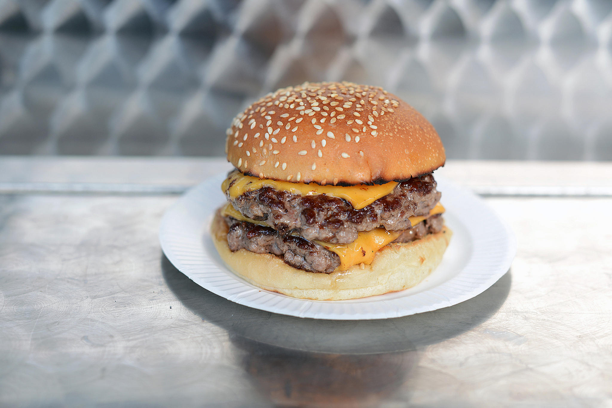 A double cheeseburger on a white plate, sitting on a stainless steel counter.