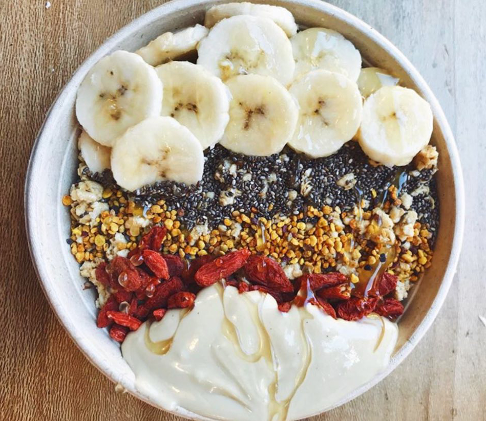 A bowl full of sliced bananas, chia seeds, granola, dried fruit, and yogurt drizzled with honey