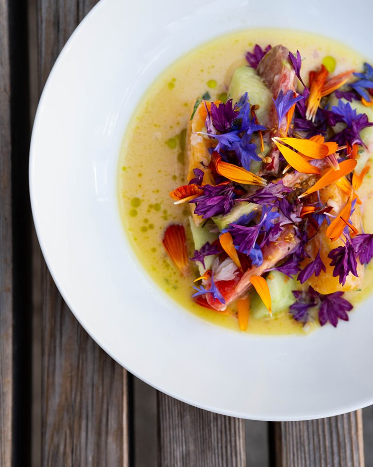 Heirloom tomatoes and bright flowers in a bowl with broth