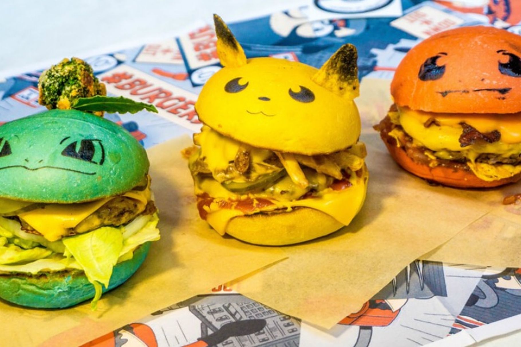 A photo of three burgers with buns that have been dyed green, yellow and orange and drawn-on and attached features, including eyes and ears, that make them look like Pokémon