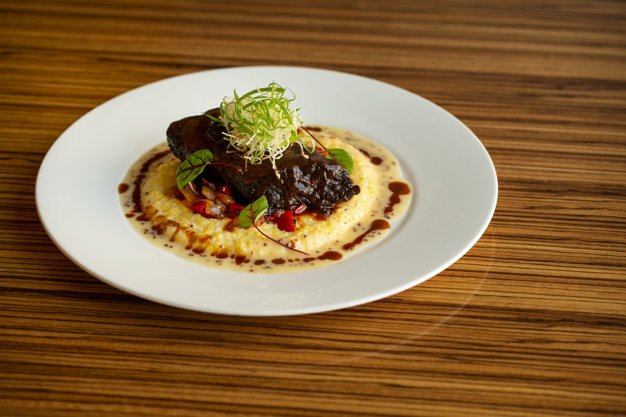 A plate of tamarind glazed angus short rib with Wade’s mill corn grits, ratatouille, crispy taro, and Ghent mustard emulsion.