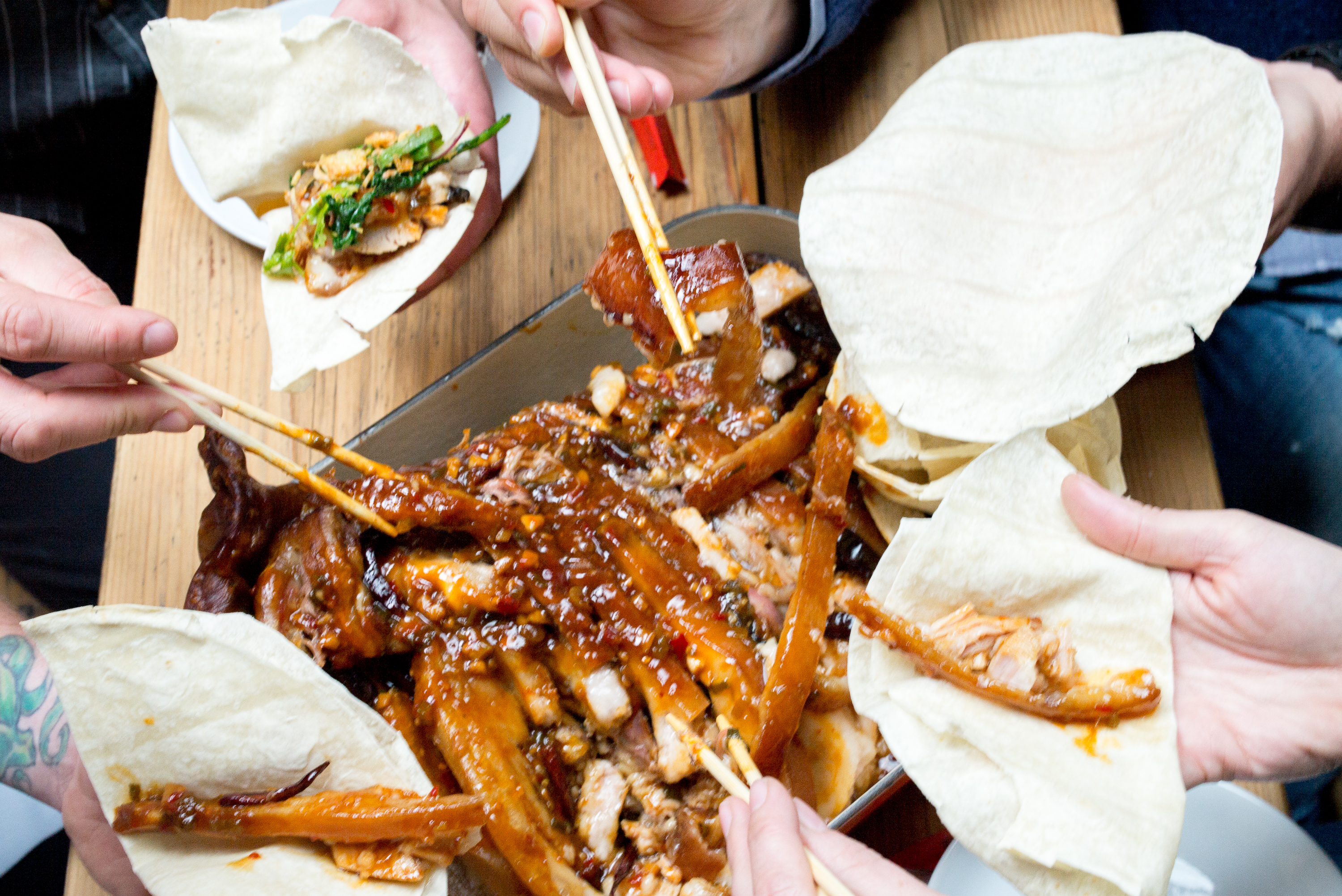 Several people digging into a roasted pig’s head with chop sticks