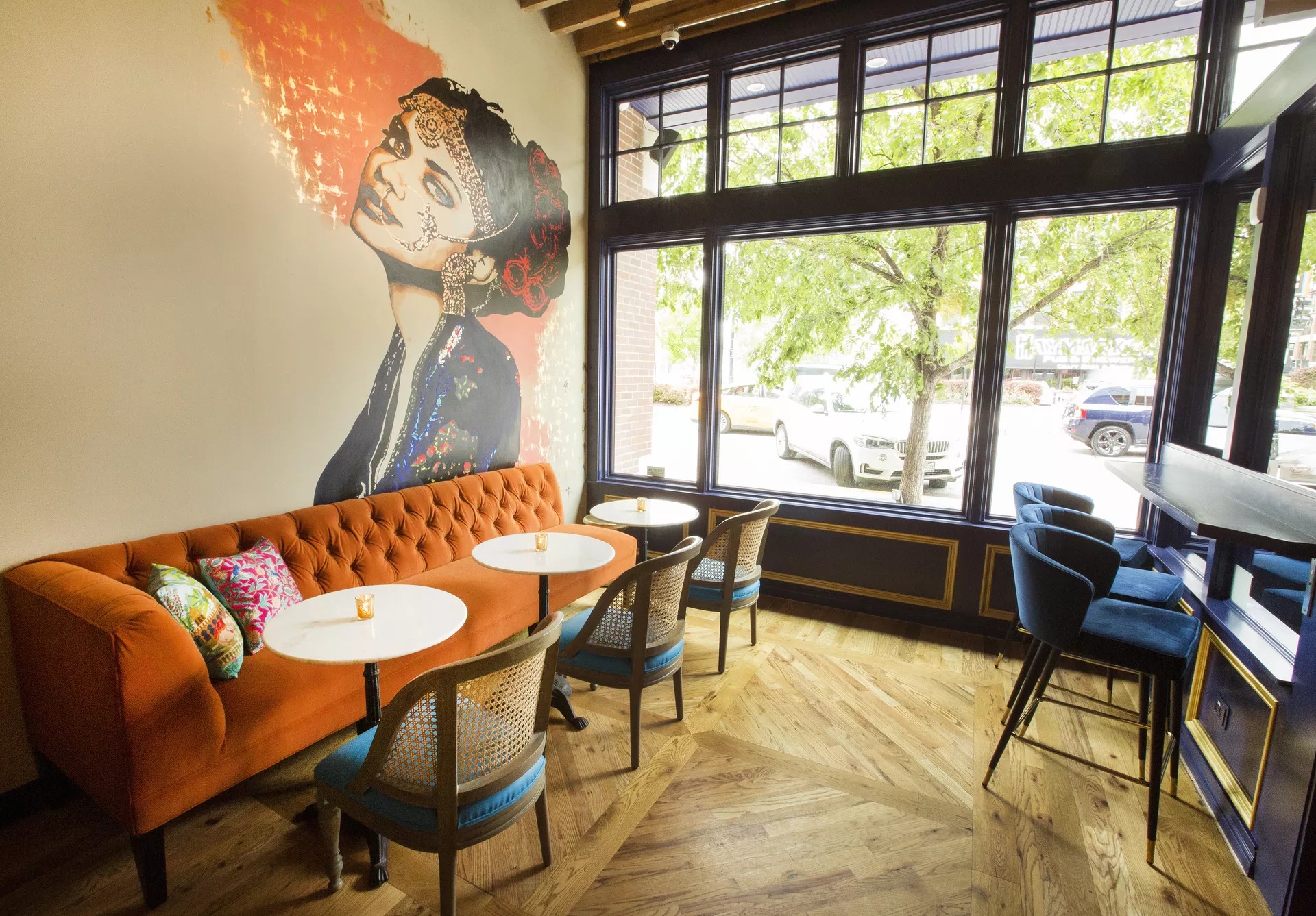 Rooh’s dining room features high top seating, an orange couch, and a painted mural called Christine by Jenny Vyas,