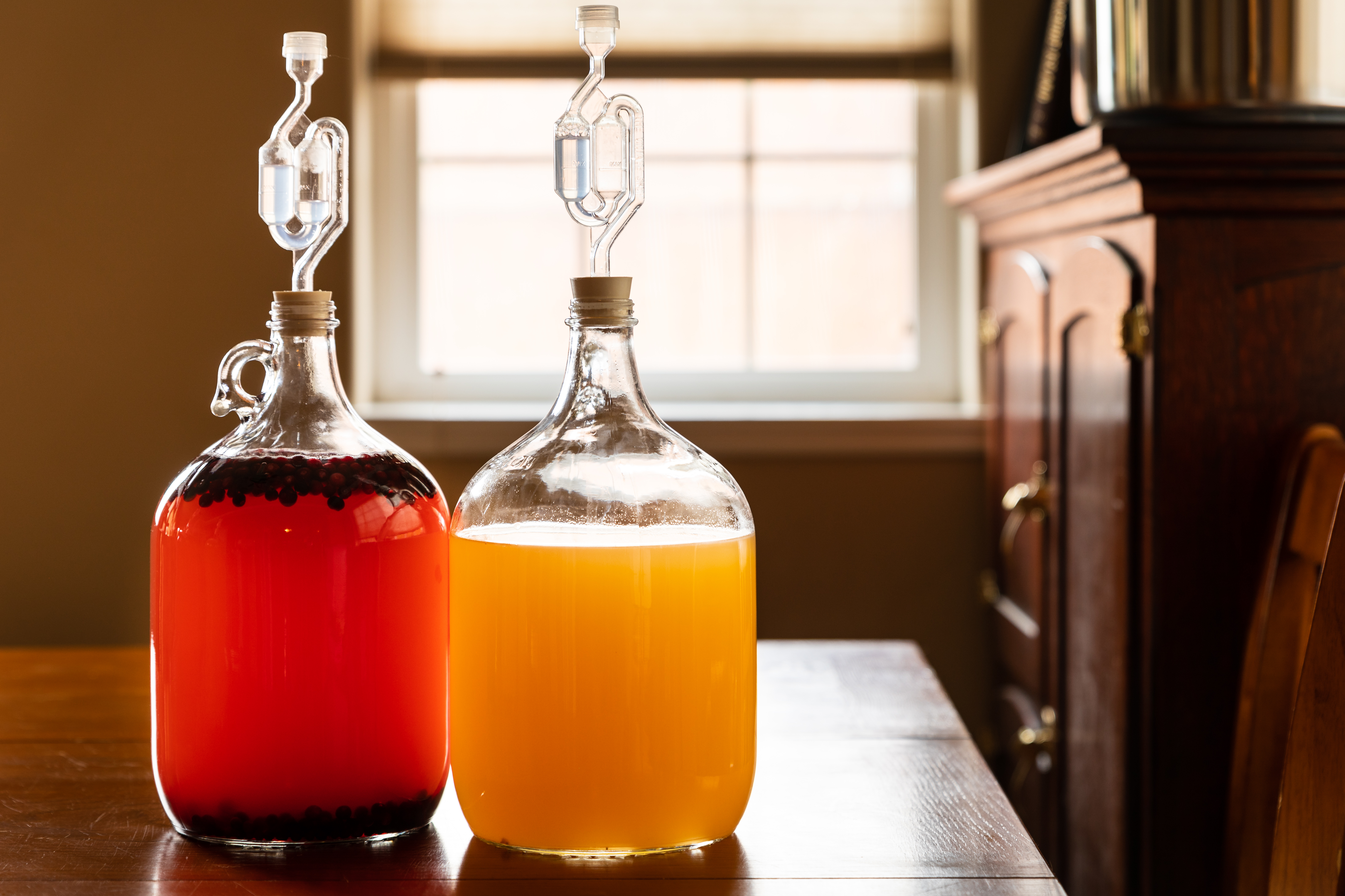 Two big glass jugs contain golden mead and pink mead.