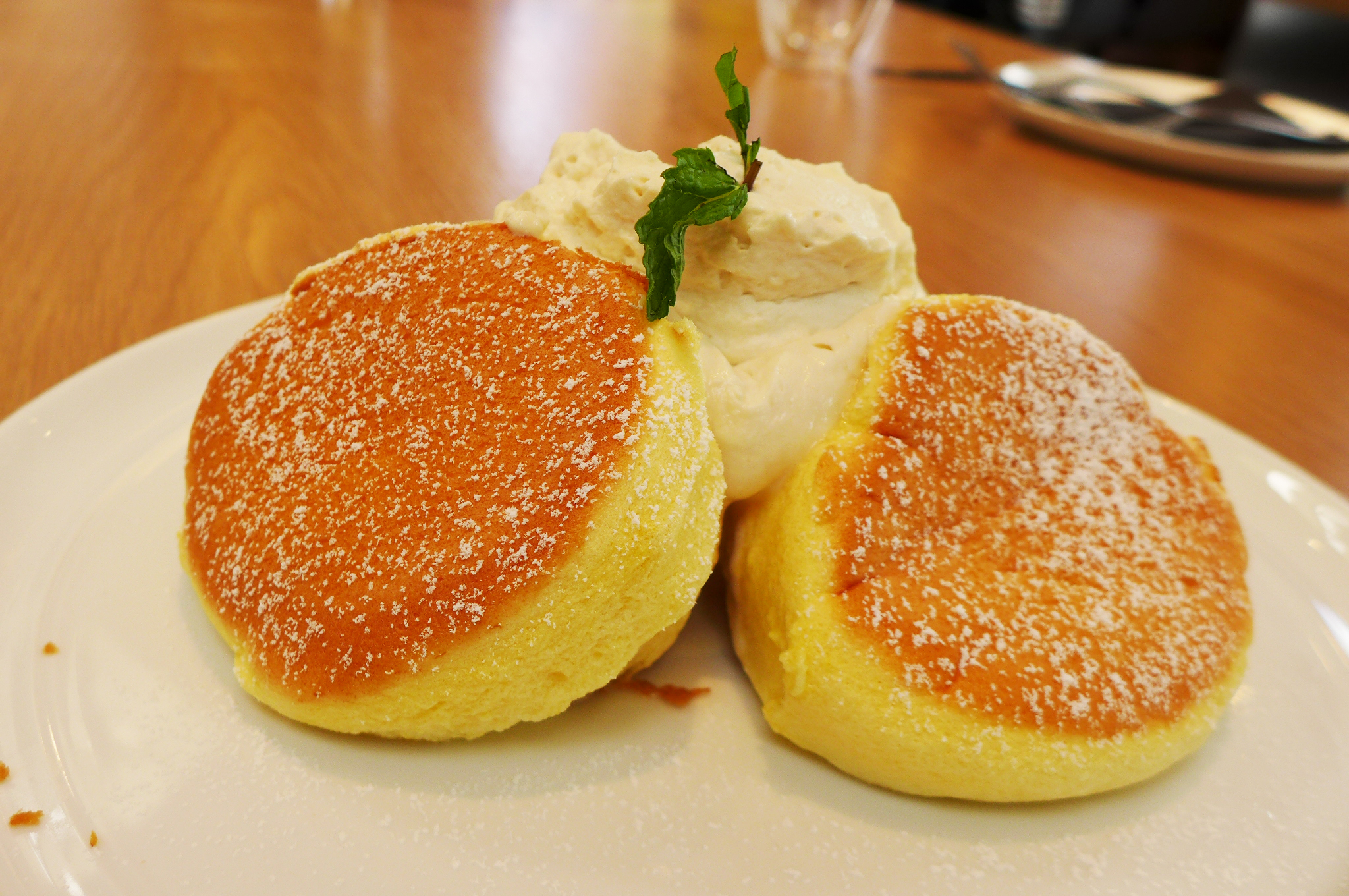 Two round puffy pancakes browned on top with a cloud of whipped cream behind them and a sprig of fresh mint on top...
