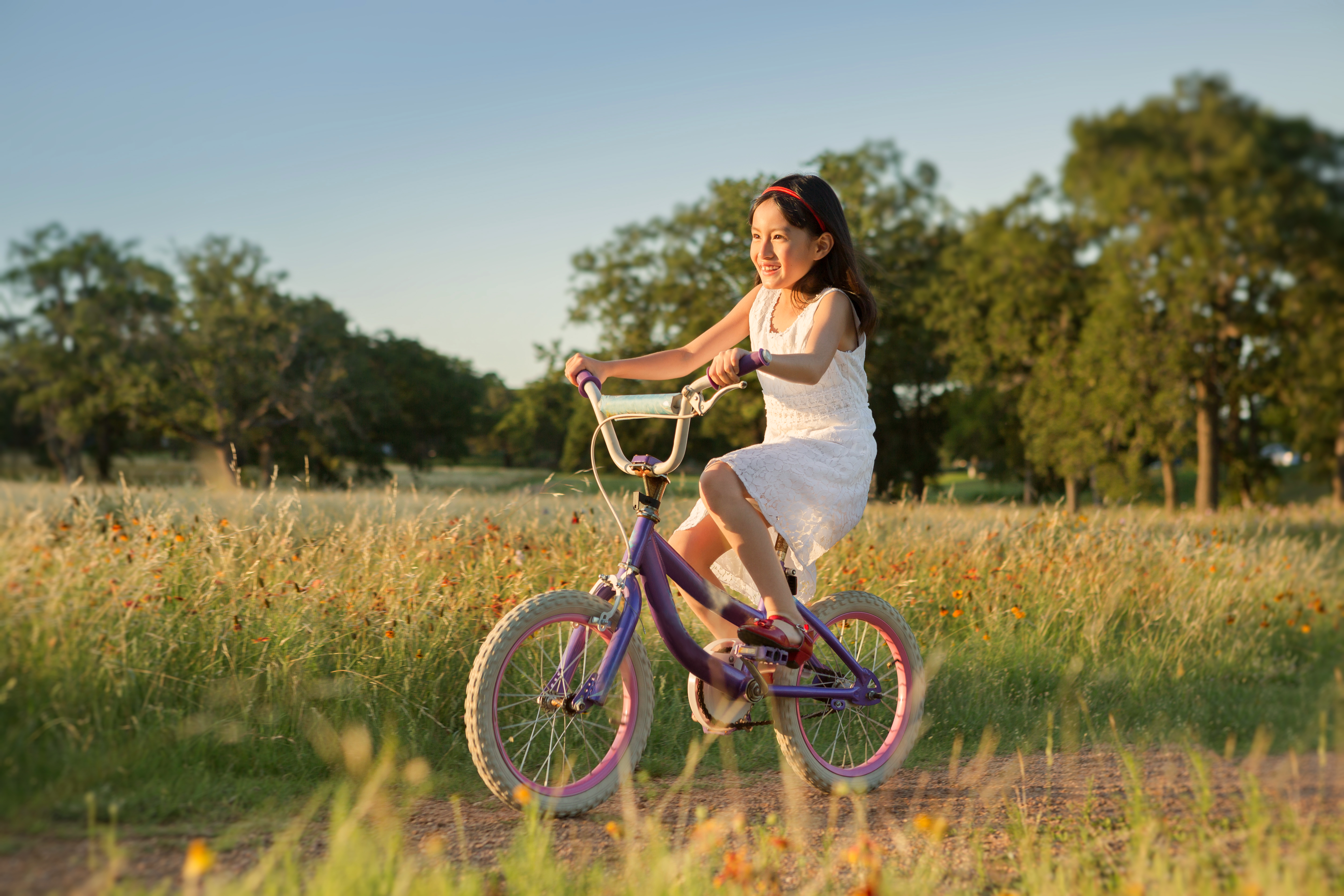 Smiling girl with light brown skin on a pink bike riding in a field.