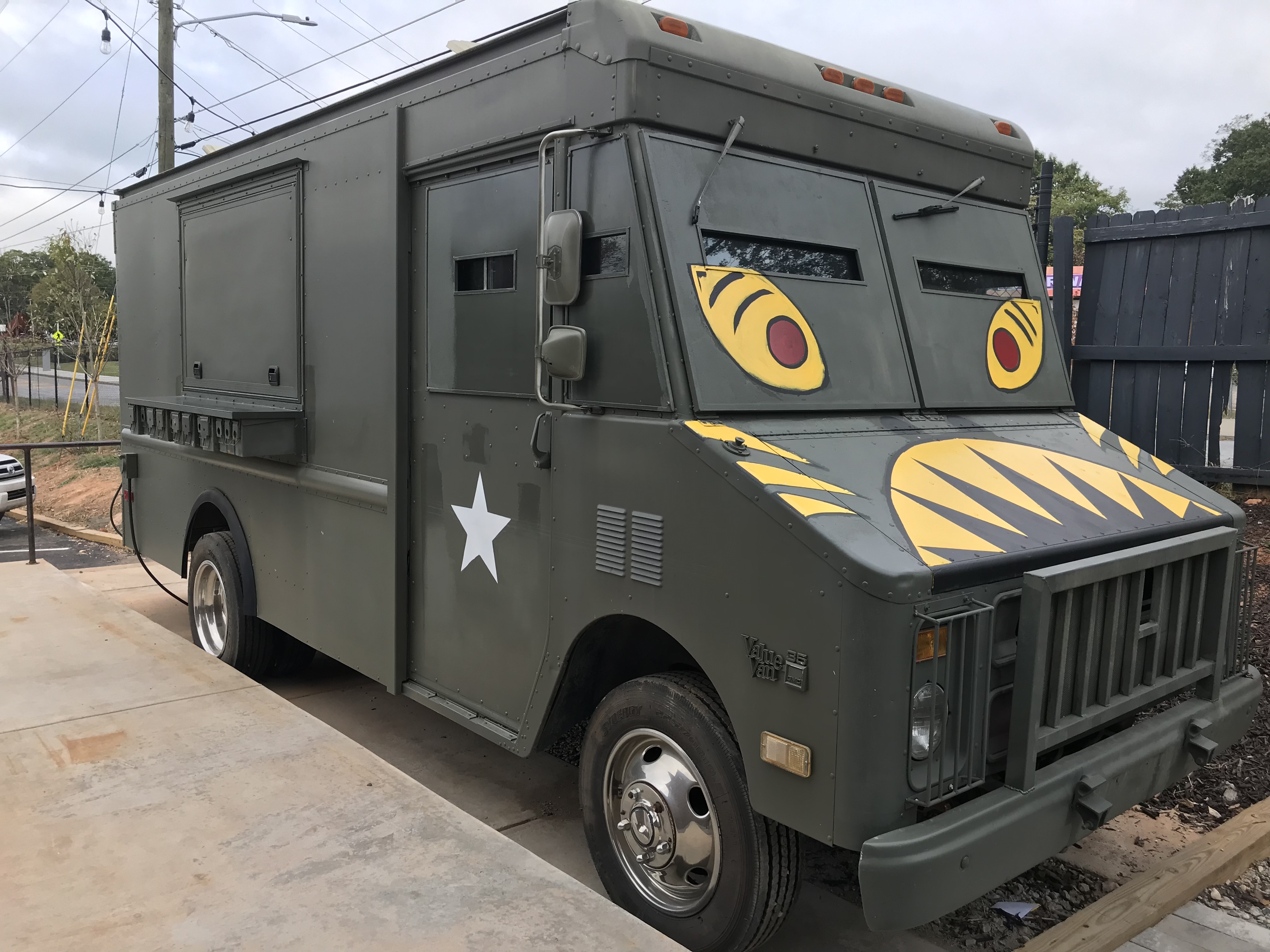 The army green Gaja Korean food truck with painted yellow eyes and teeth parked next to the patio