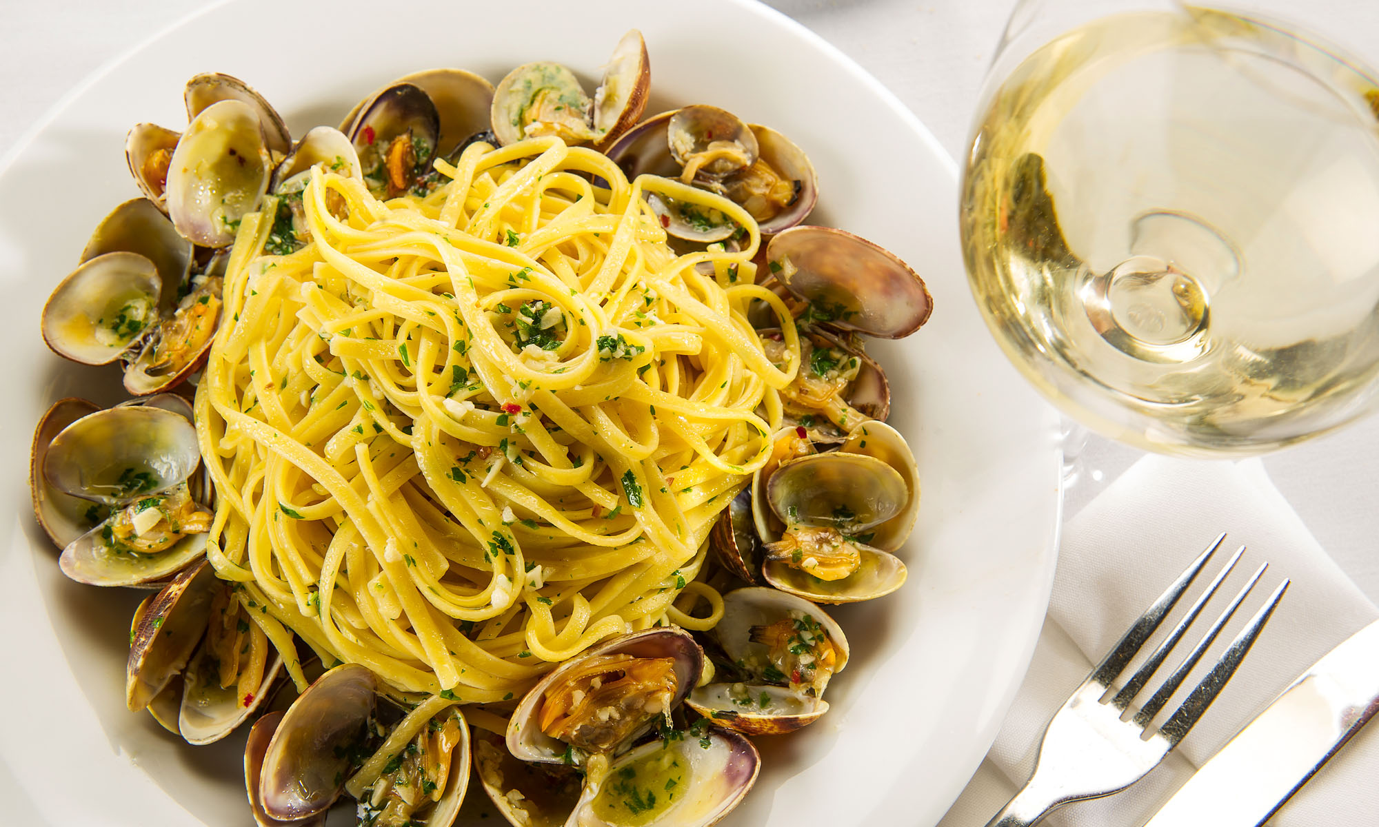 Pasta with clams on a white plate with white wine on the side.
