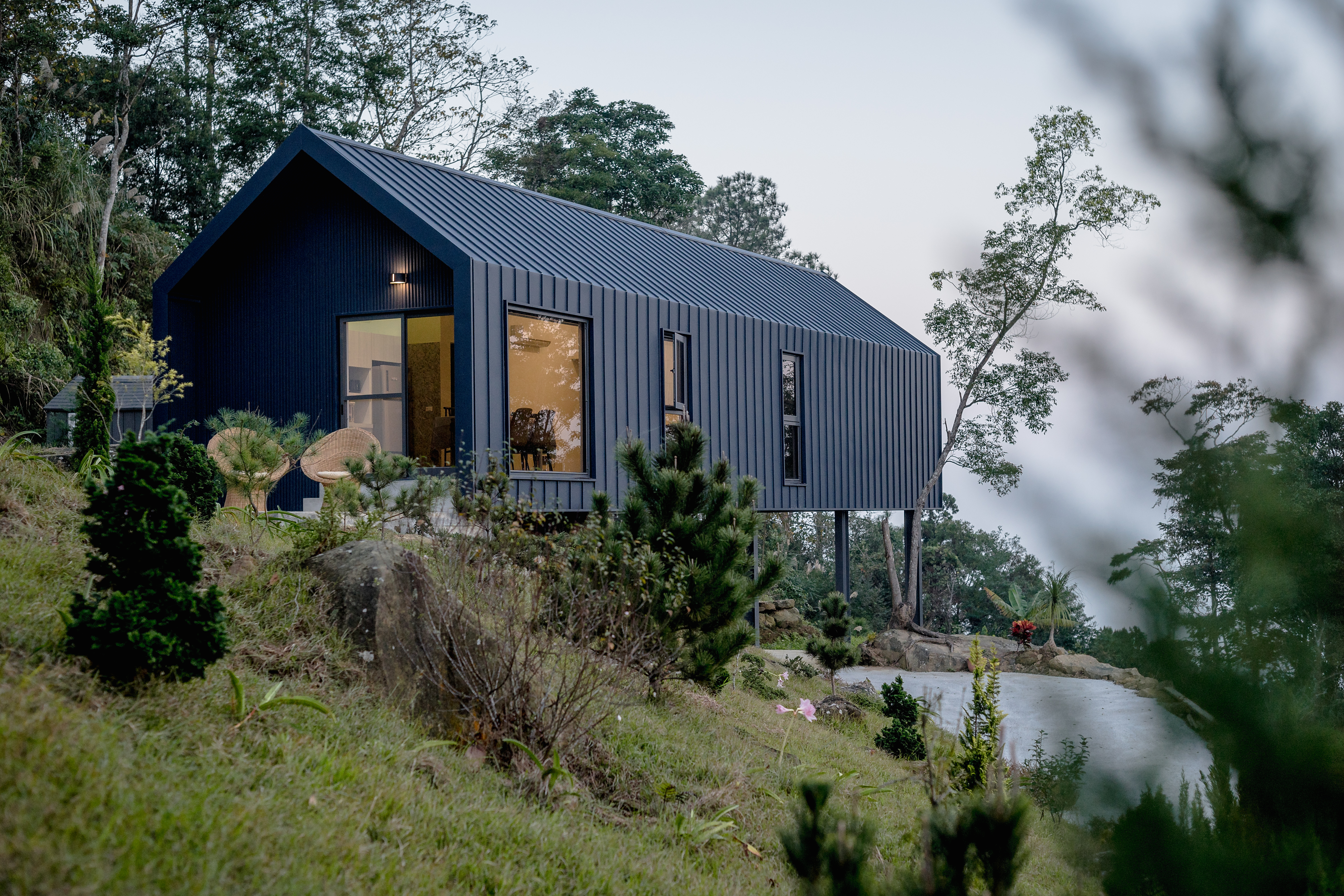 Pitch-roofed black-clad house on stilts cantilevering over mountain.