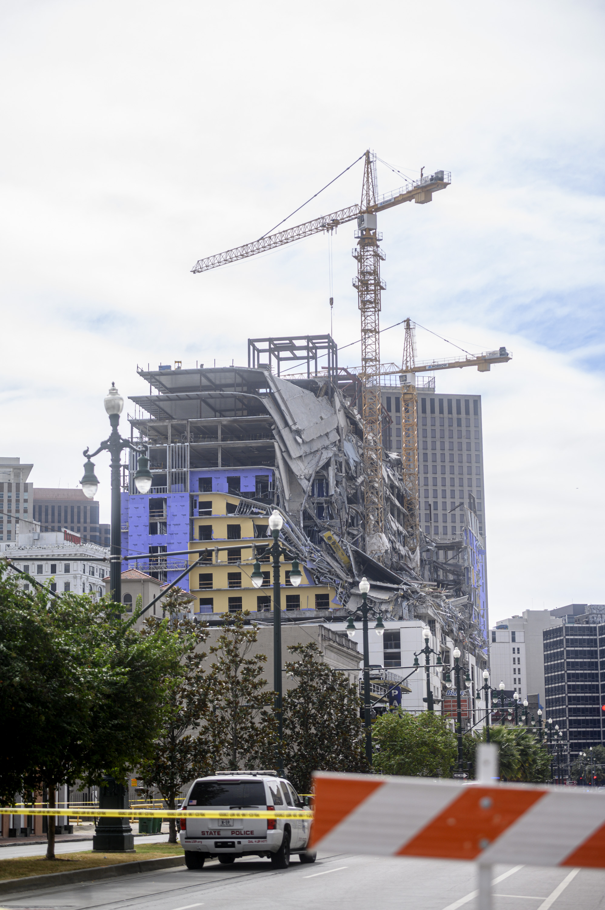 A collapsed hotel with two large cranes hovering above it faces Canal Street