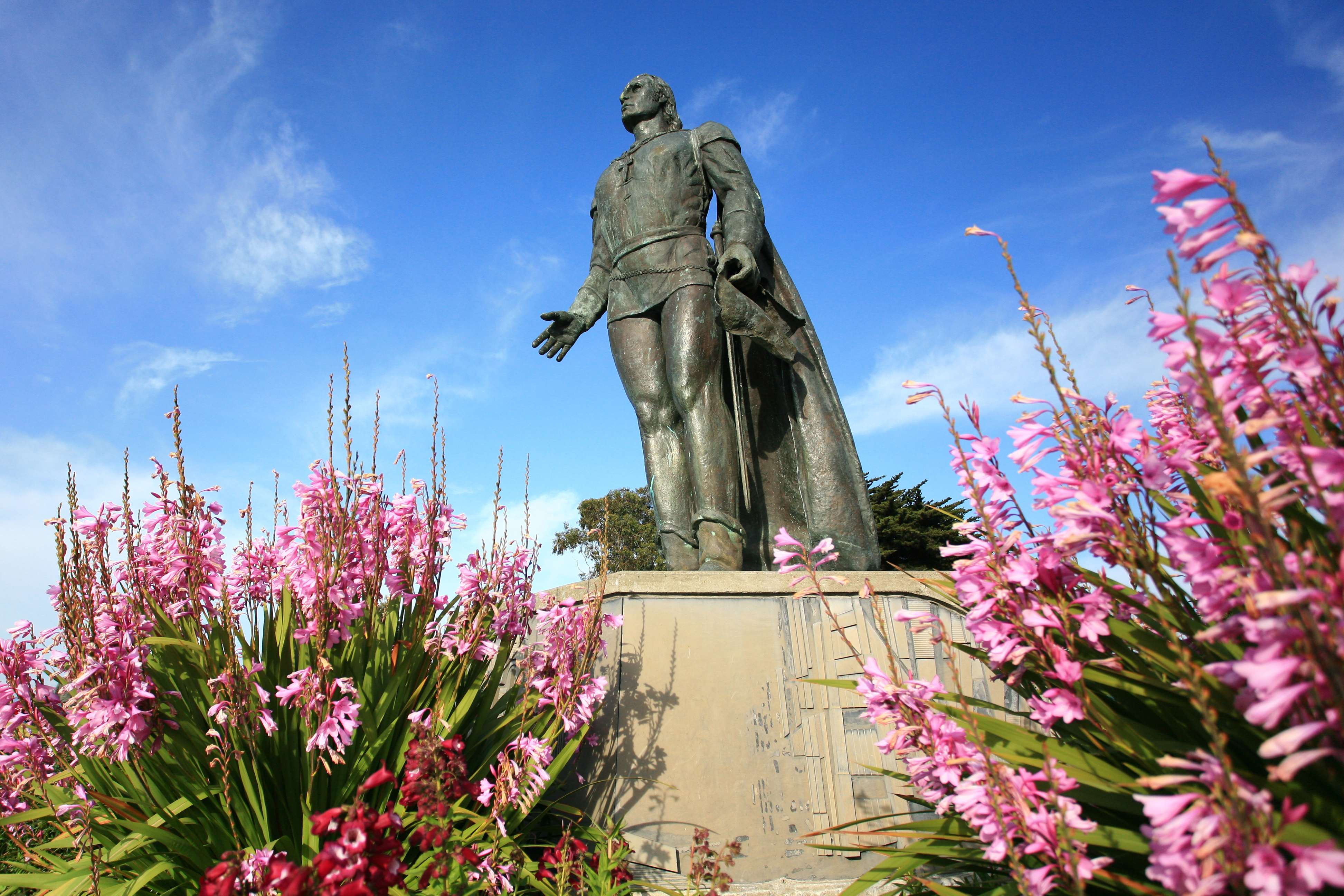 A low-angle photo of the Columbus Statue next to Coit Tower with a blue sky in the background.