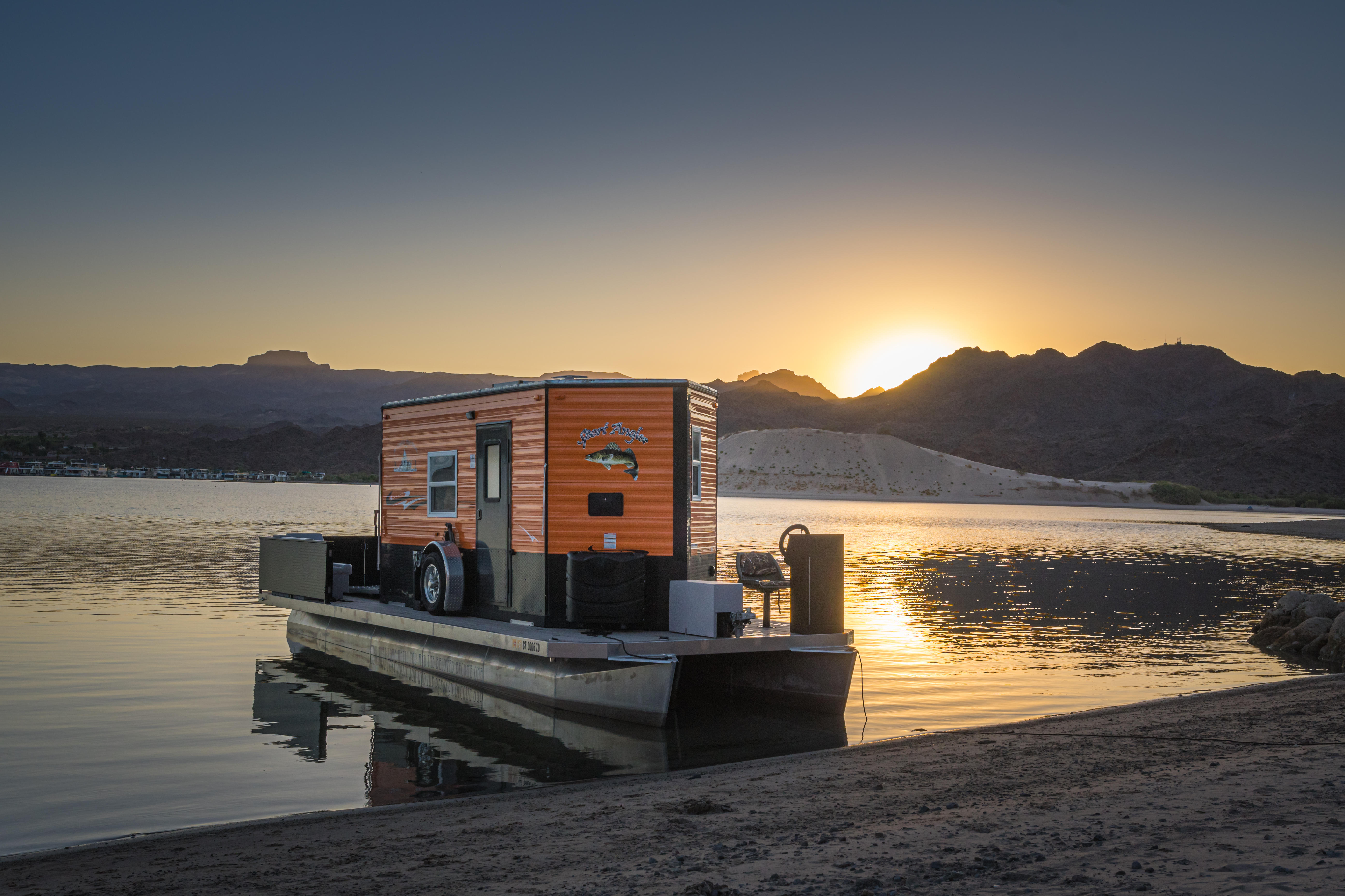 An orange trailer sits on a pontoon-style boat in the water with mountains in the background and the sun setting.