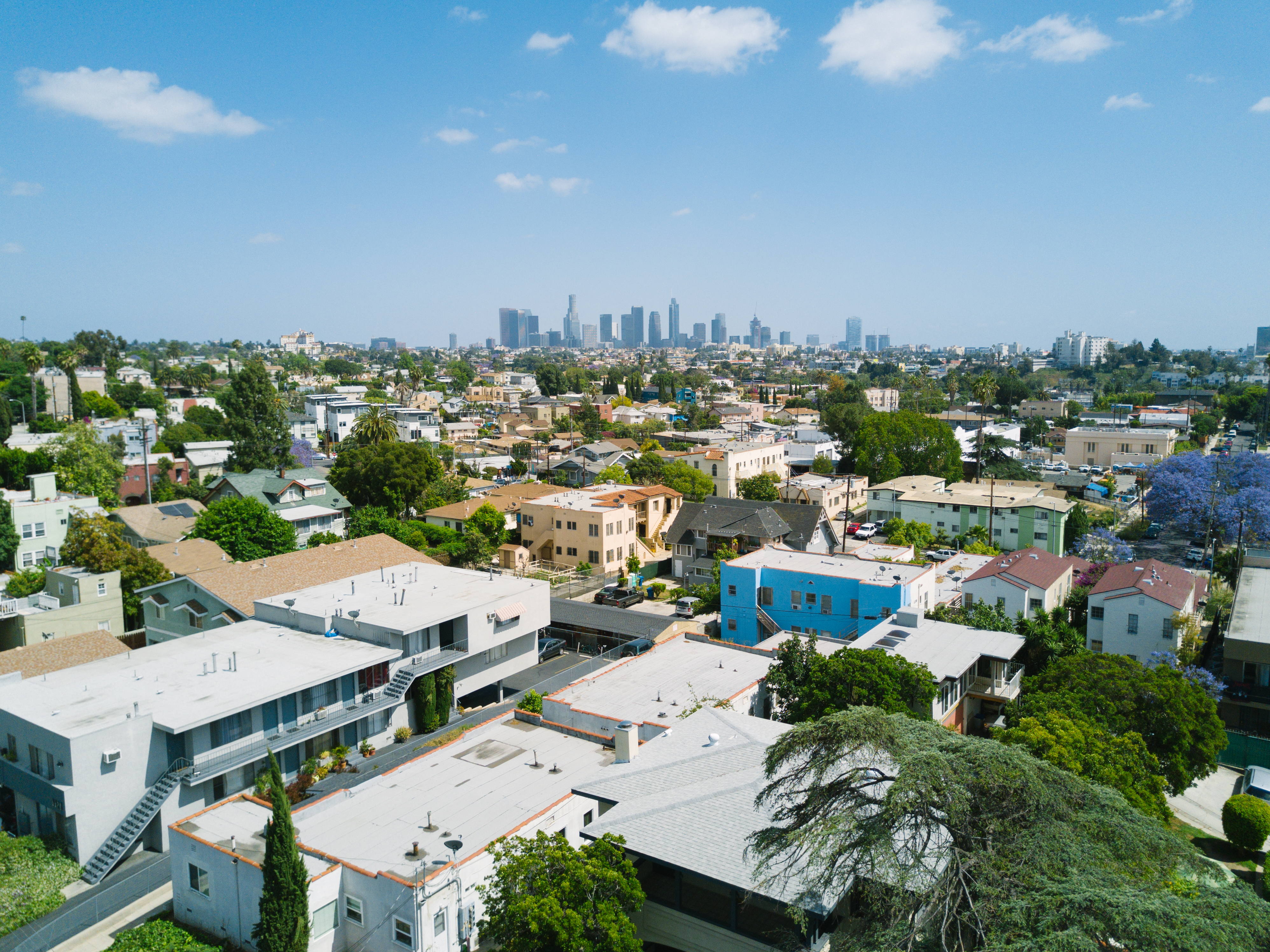 Aerial view of a dense residential neighborhoods sprawled out in front of Downtown Los Angeles. A cluster of skyscrapers poke out in the distance.