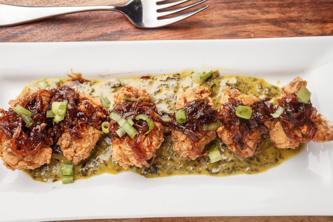 A plate of fried oysters over creamed spinach topped with scallions and caramelized onions