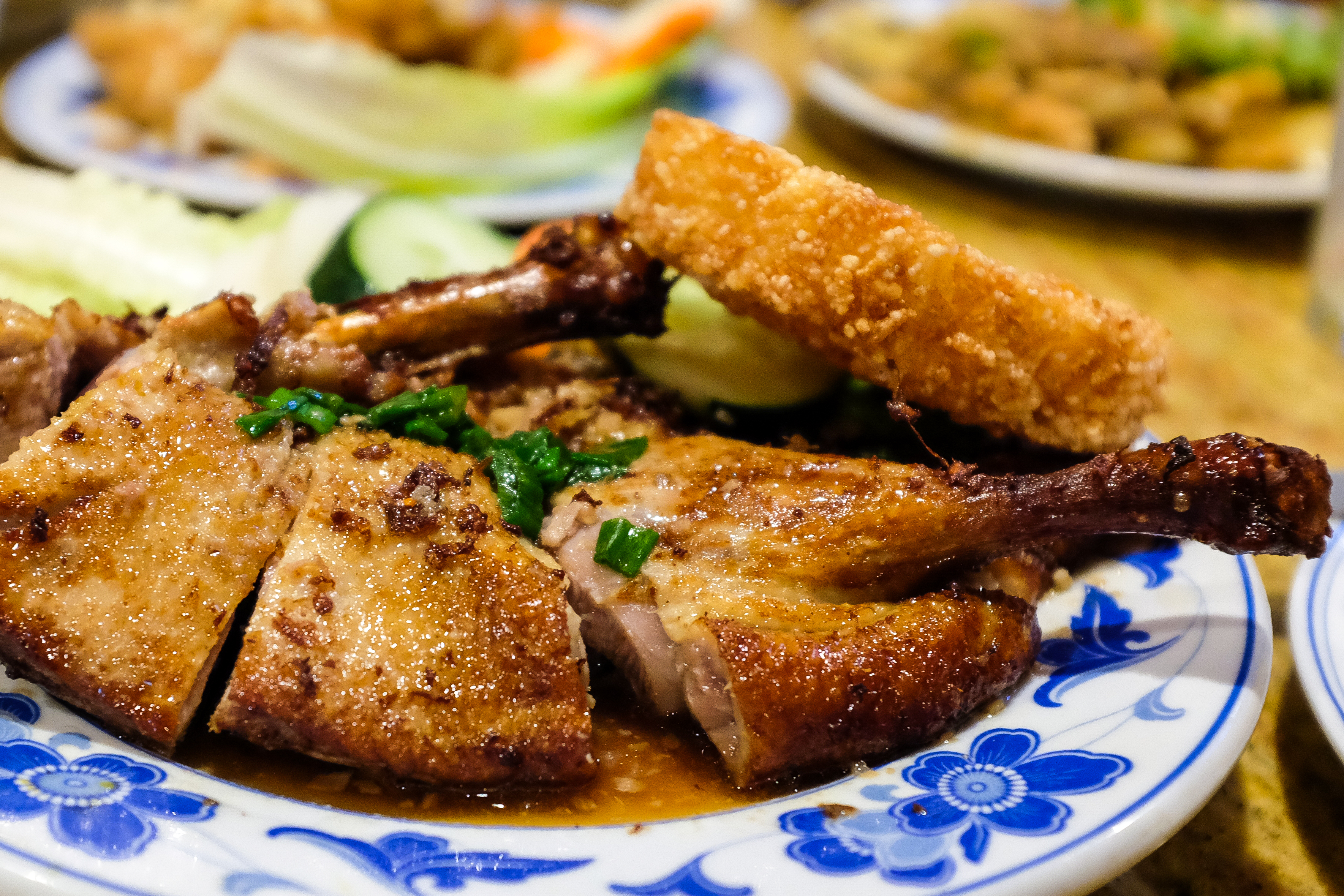 A blue and white plate of crispy roasted duck next to cucumbers and topped with a fried rice patty.