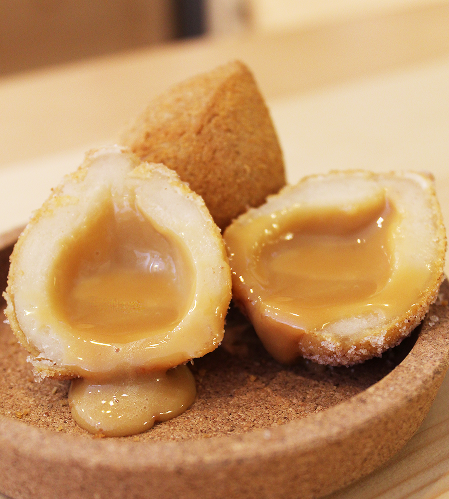 A tear drop-shaped fried dough pocket cut in half, with caramel oozing out