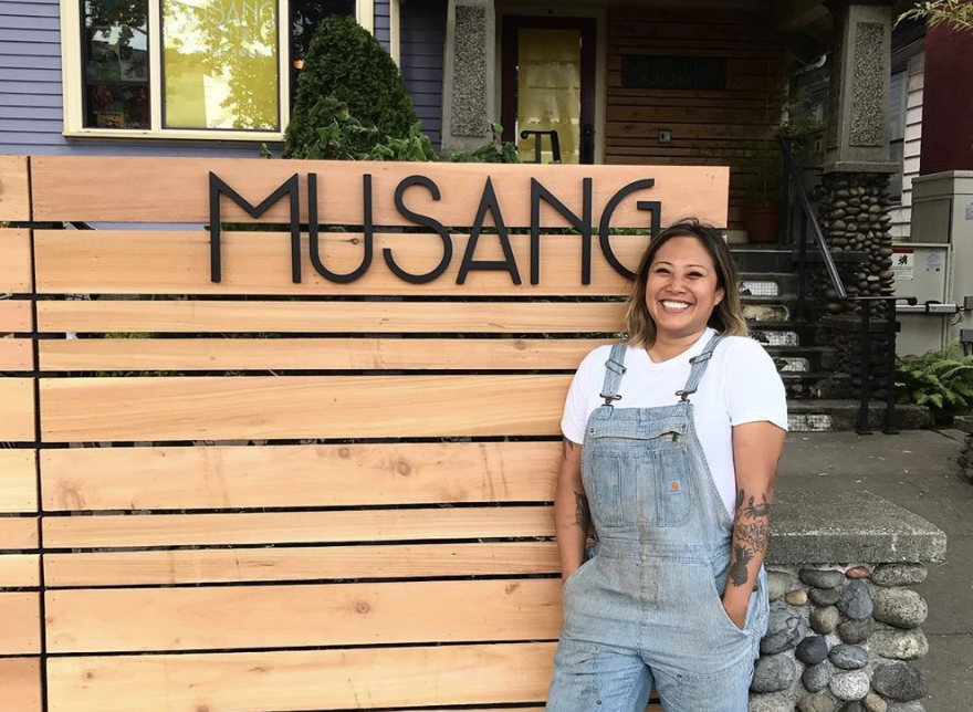 The sign in front of Musang against light wood, with chef Melissa Miranda standing next to it.