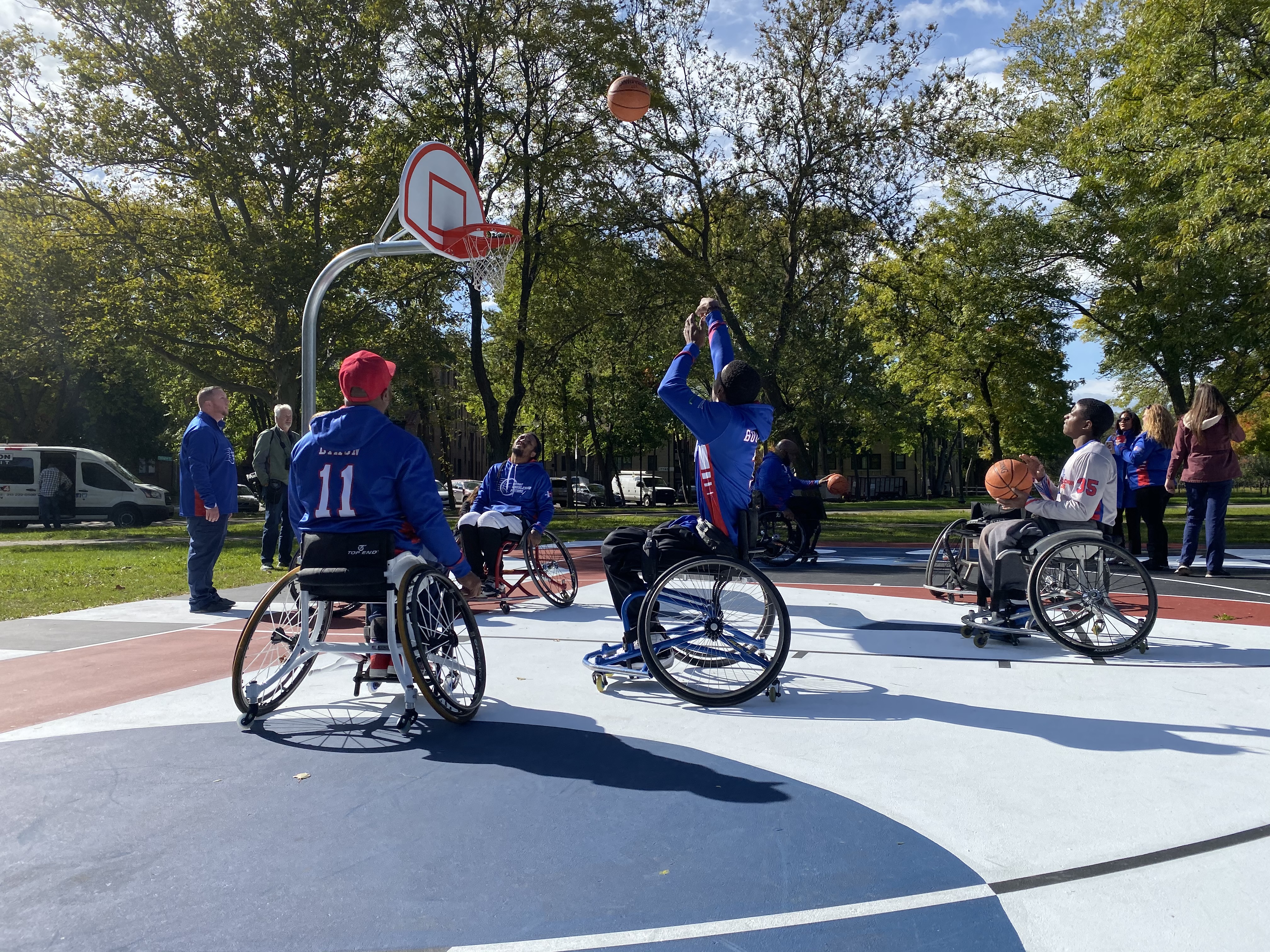 A group of men in wheelchairs play basketball on a court with fresh paint of blue, white, and red.