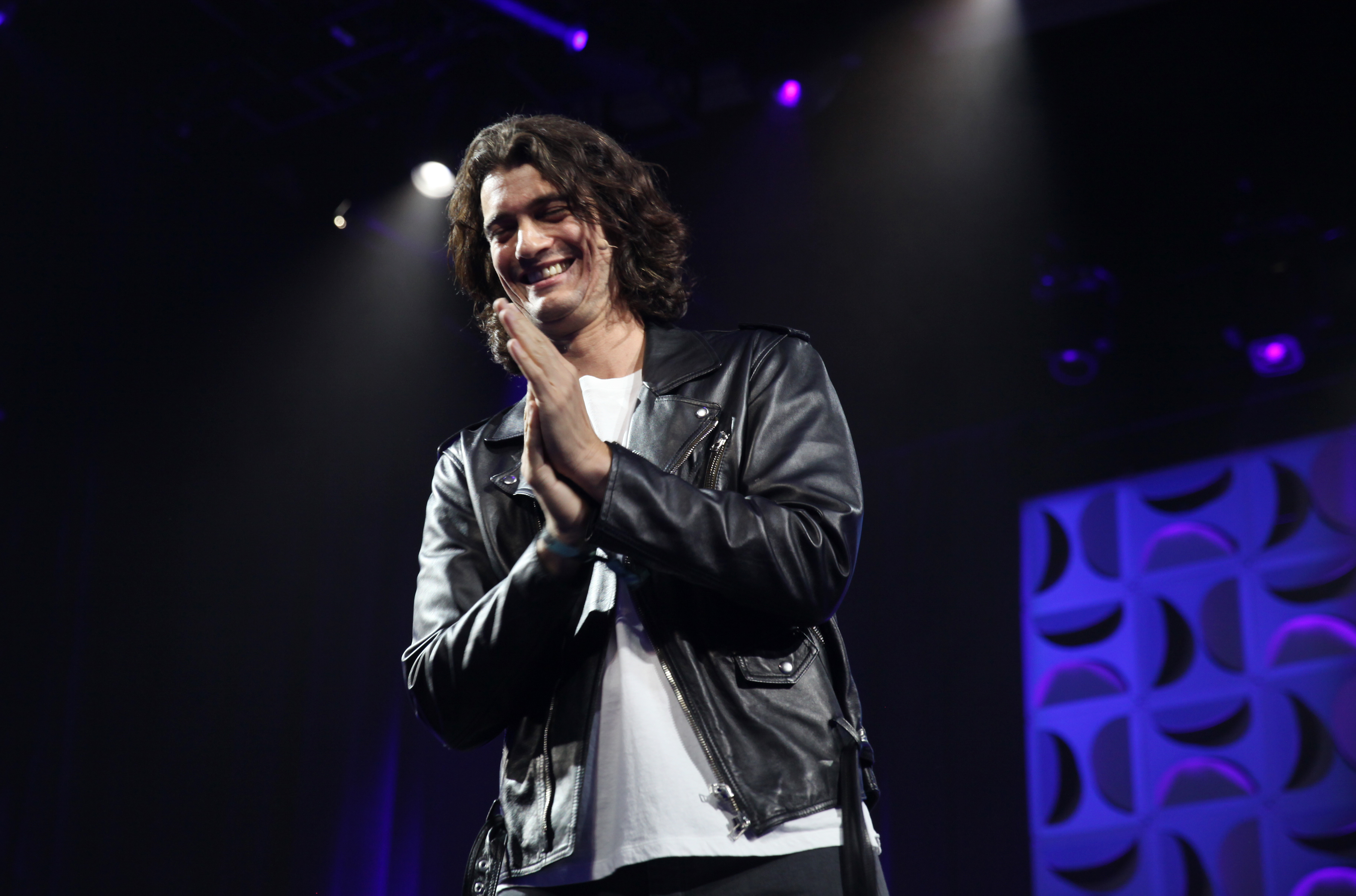 WeWork’s ex-CEO Adam Neumann clasps his hands and smiles at the audience from onstage.