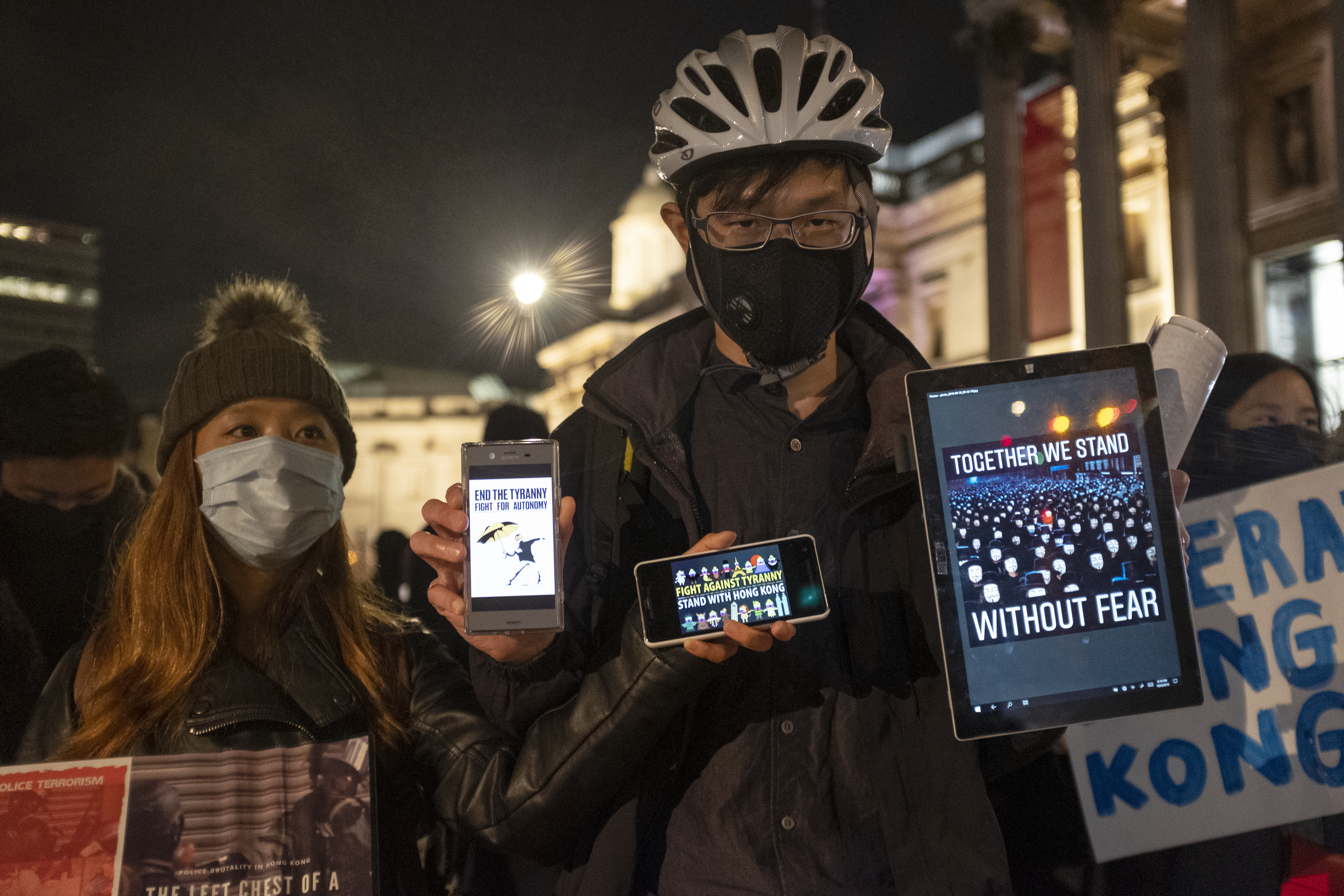 Man and woman in face masks holding phones and a tablet are protesting against the implementation of new laws by the Hong Kong government that forbid protesters from wearing masks in a public protest.&nbsp;