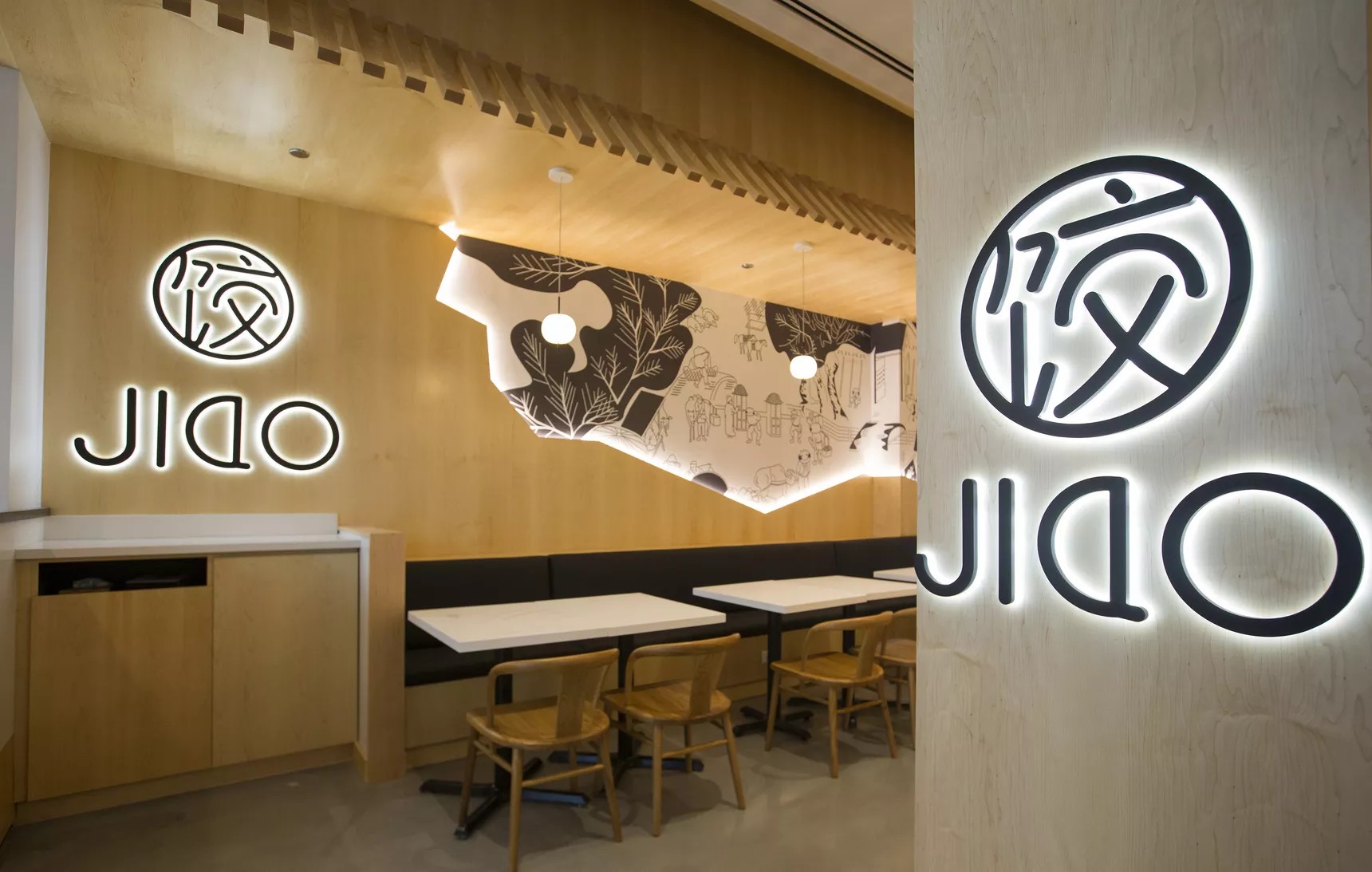 A dining room entrance with blond wood and large black signs that read “JIAO.”