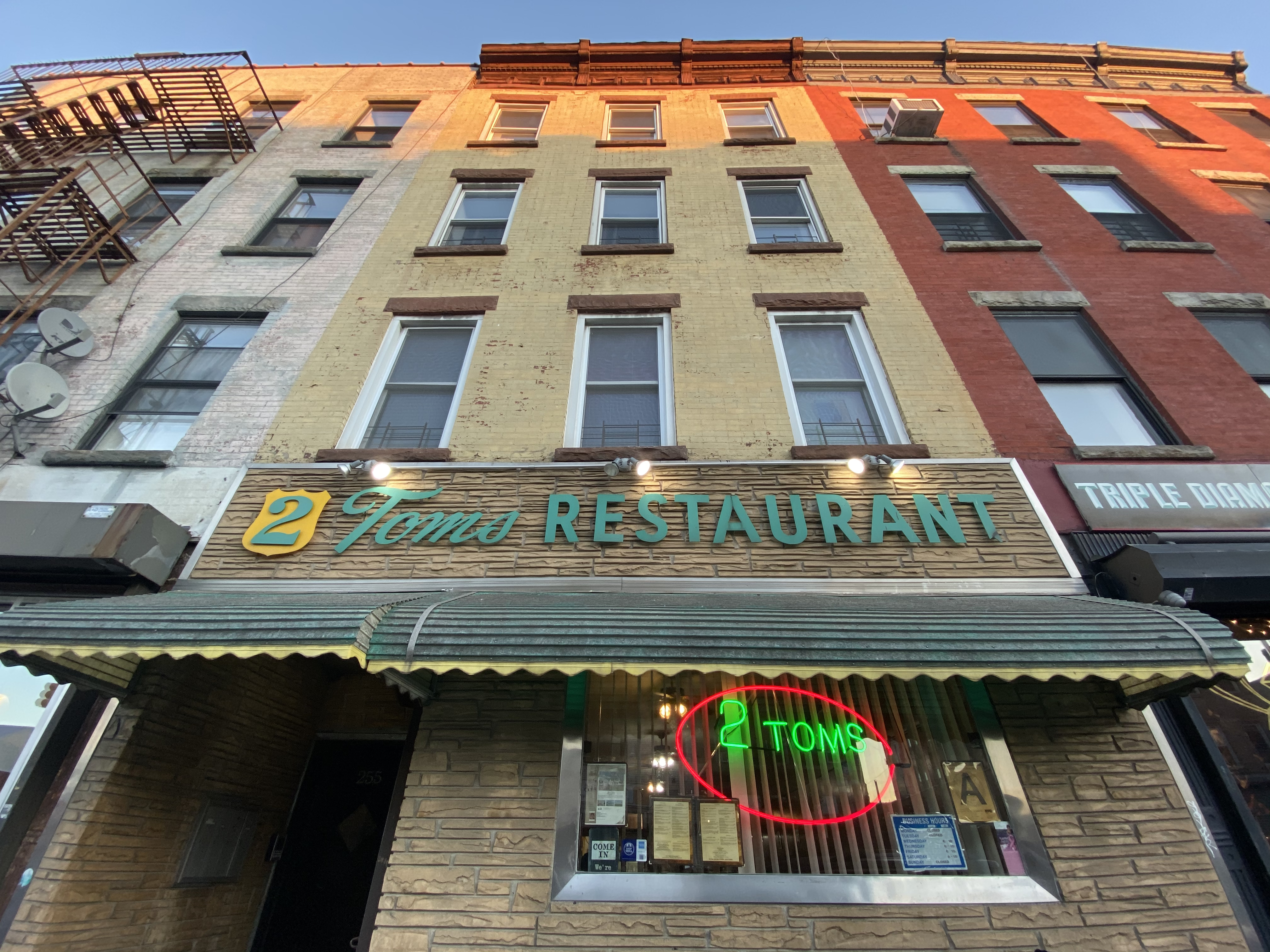 A neon sign shins near the entrance for Two Tom’s, while sea green lettering hangs above the window