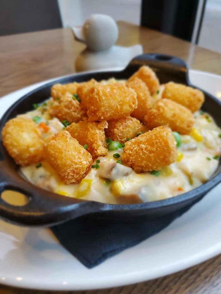 A small cast iron pan holds something creamy with visible peas, topped with tater tots
