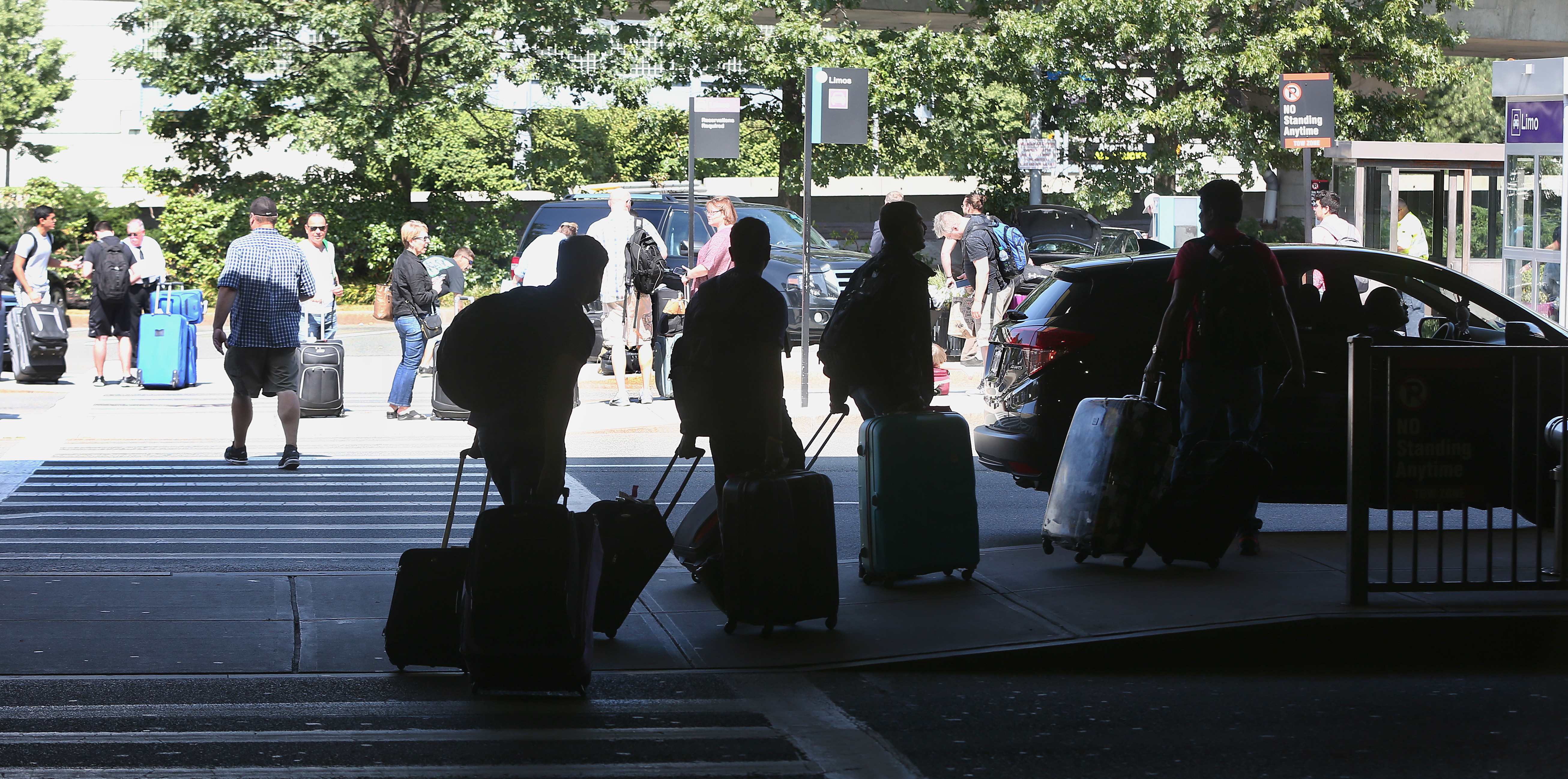 People rolling suitcases behind them as they emerge from cars at the airport.