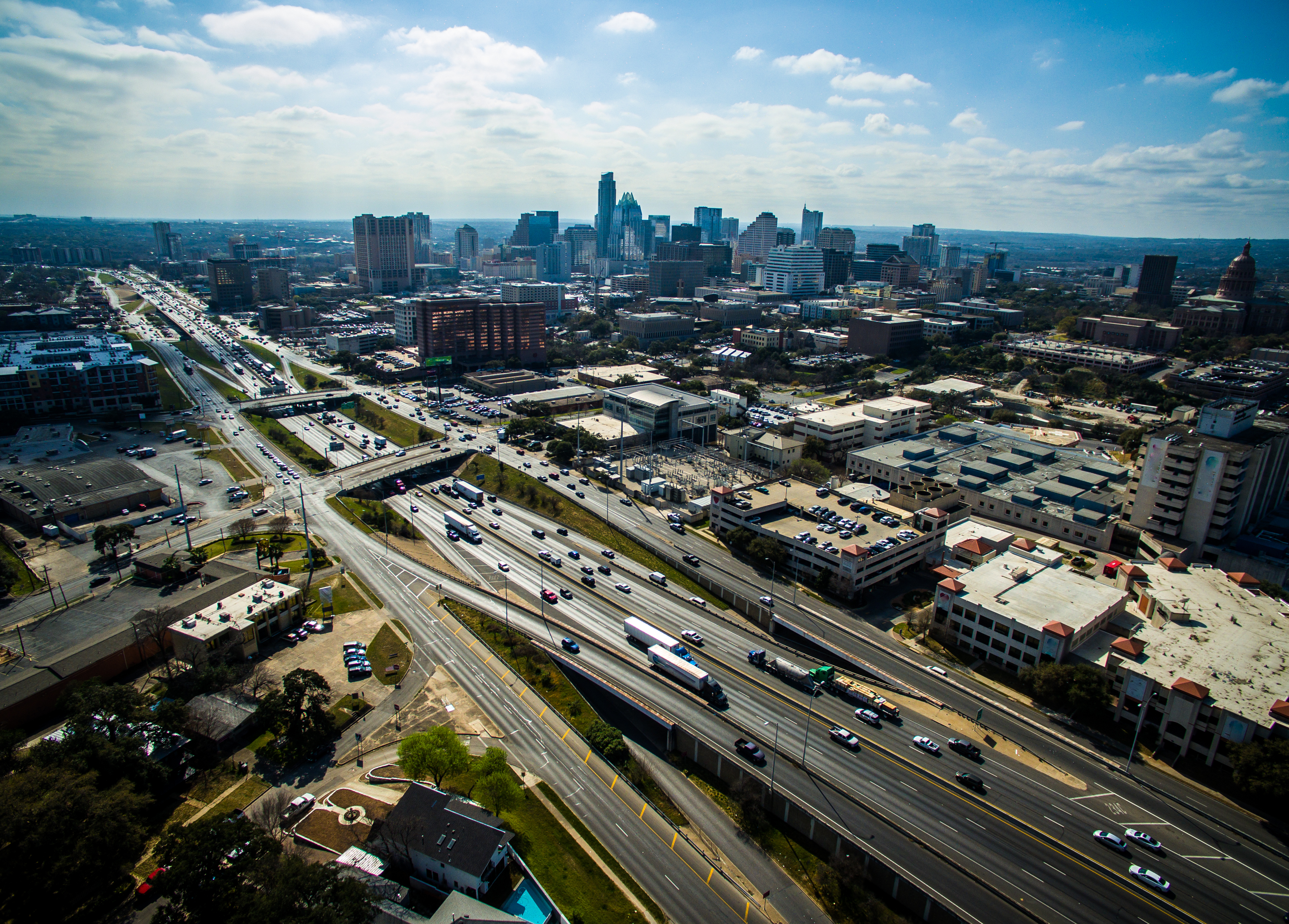 Overhead view of highways surrounded by medium-height buildings with a group of tall buildings in the background.