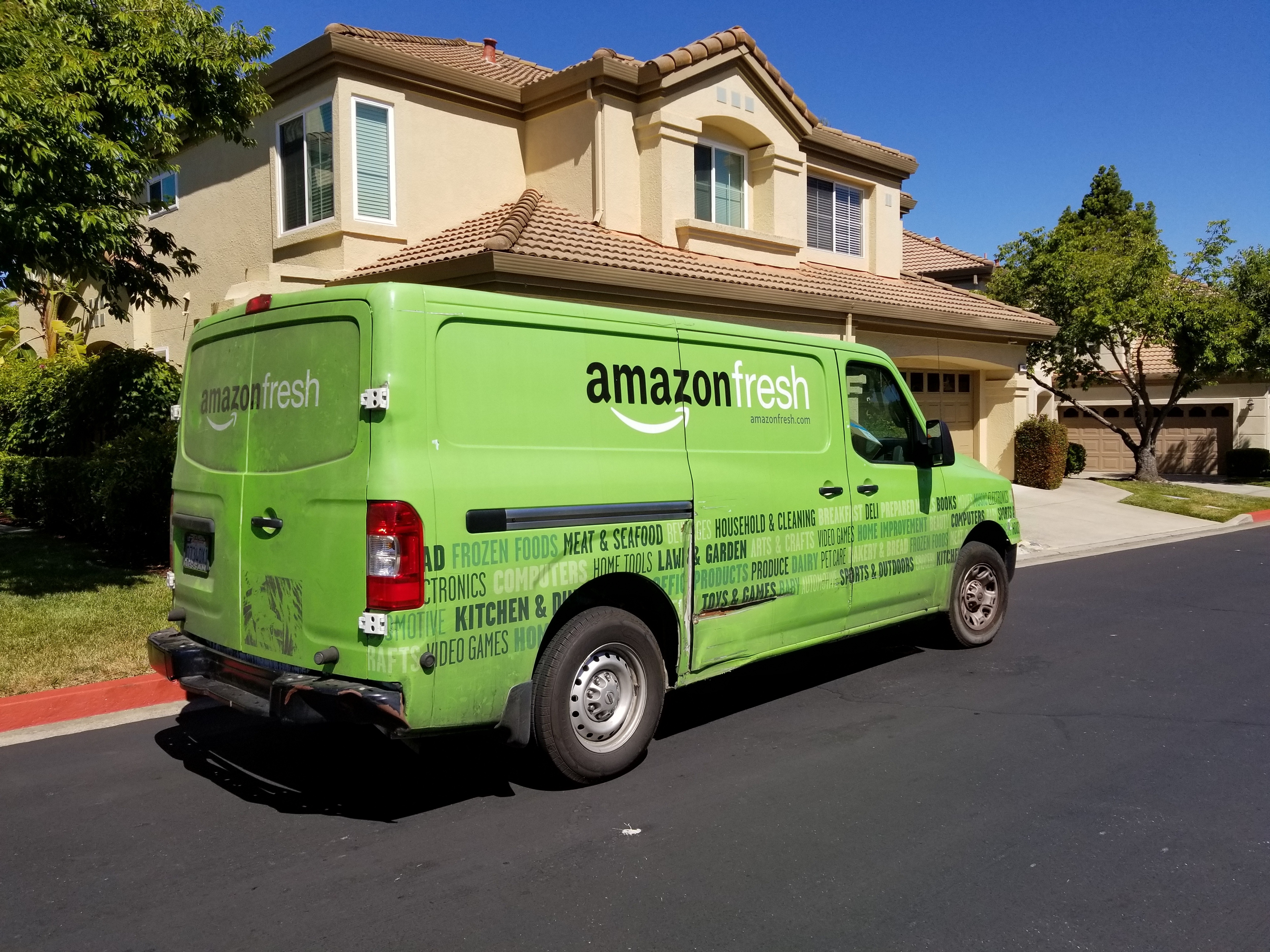 An Amazon Fresh delivery van stopped outside a suburban home.