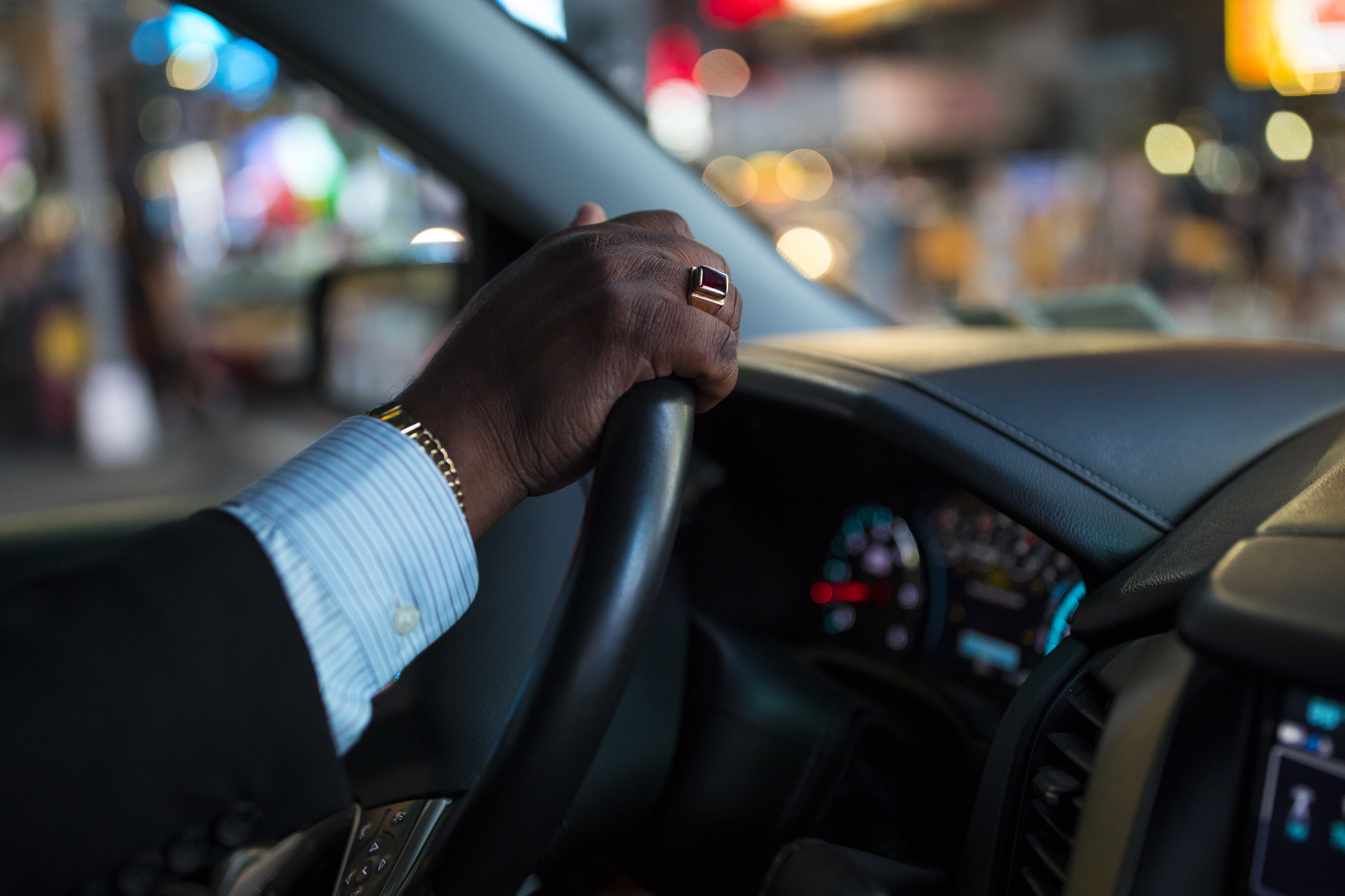 A man’s hand on a steering wheel inside a car at night.