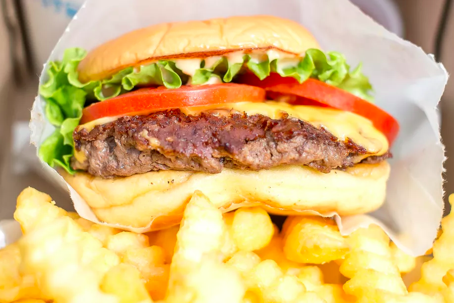 Close up of a Shake Shack burger topped with cheese, lettuce, and tomato, with crinkle-cut french fries