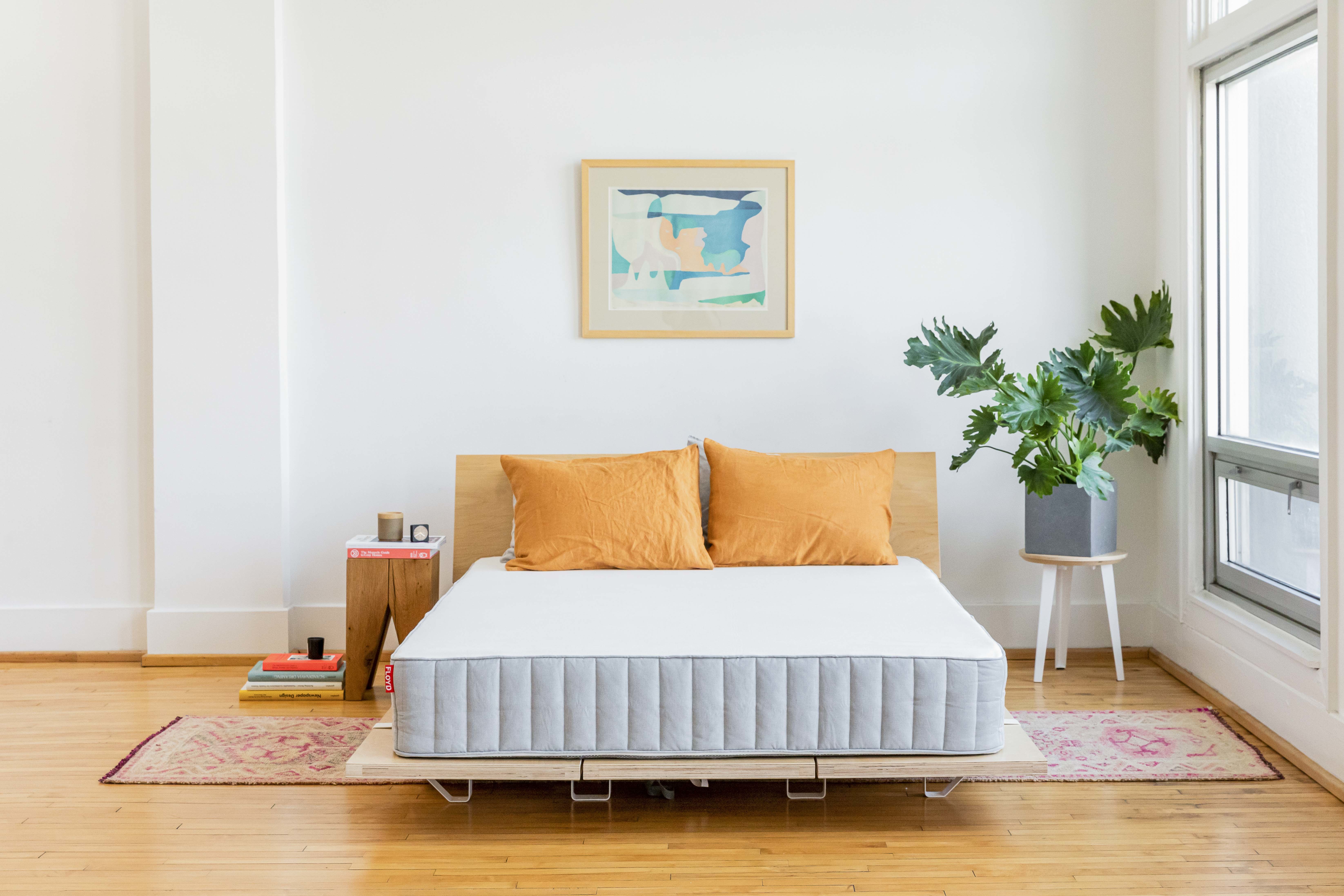 Mattress on wooden bed frame, with two orange pillows.