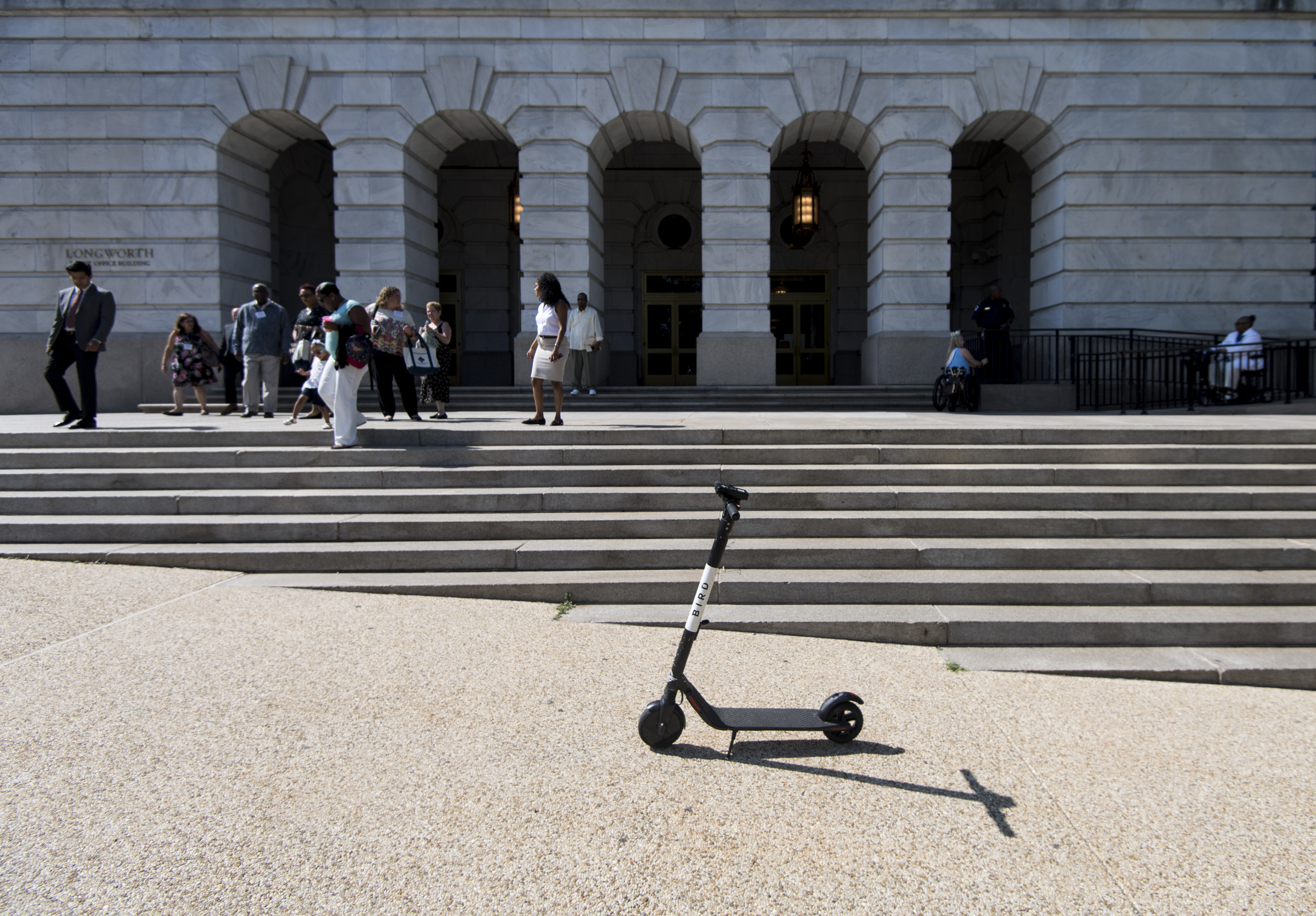 An electric scooter on a sidewalk in front of a classical building with archways.